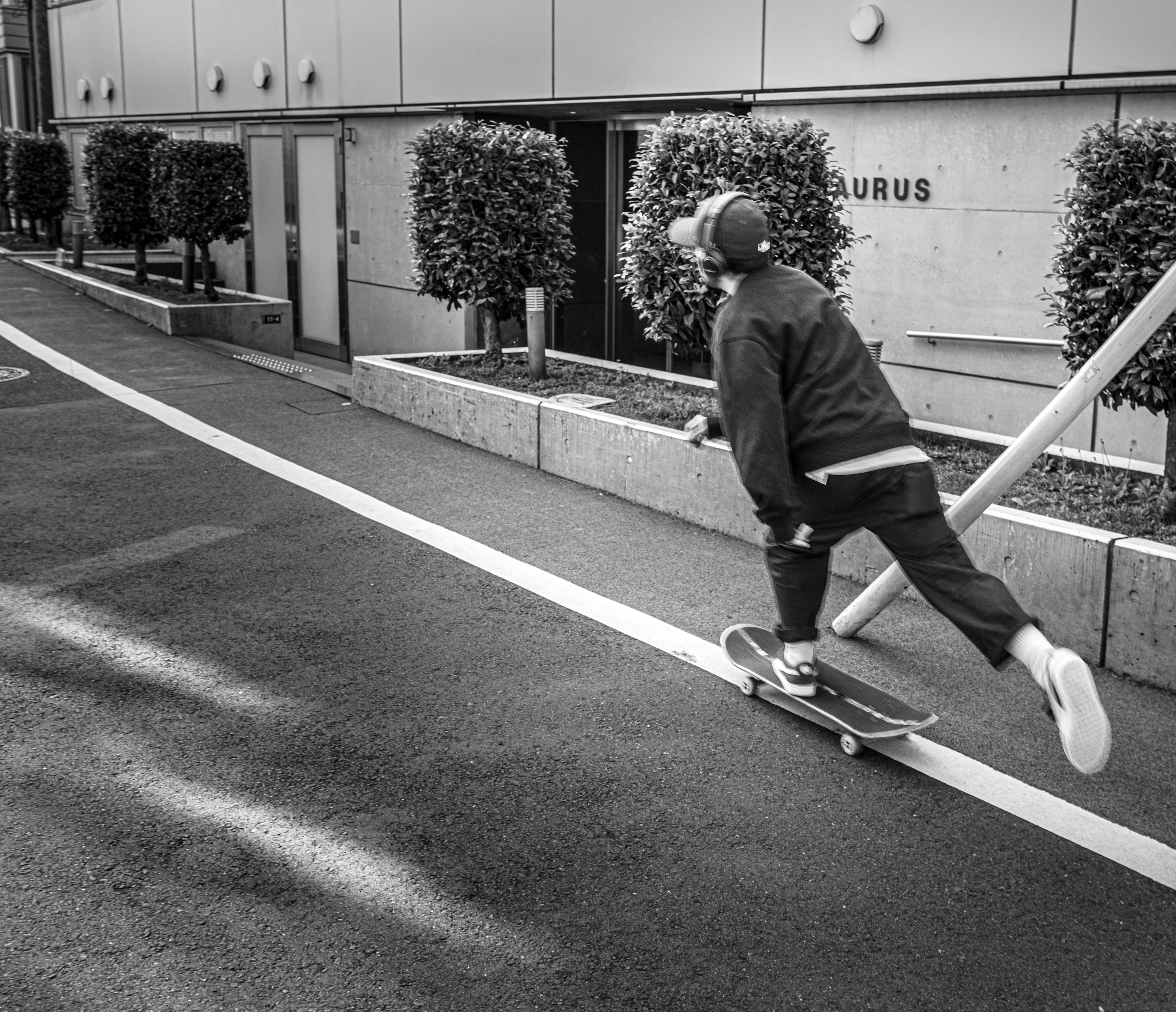 Seorang anak laki-laki bermain skateboard di jalan dengan latar belakang hitam-putih