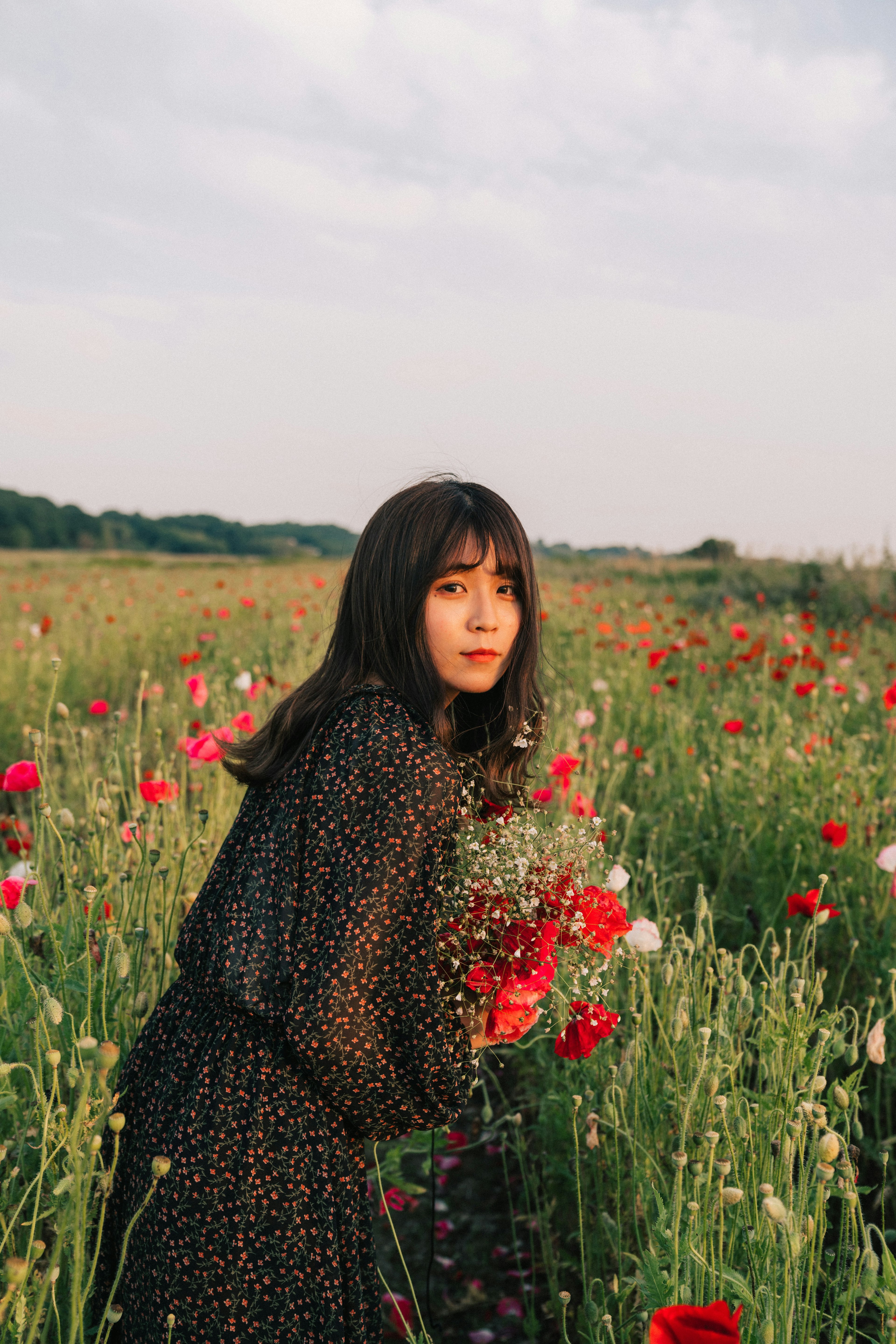 Una mujer sosteniendo un ramo de flores de pie en un campo de flores