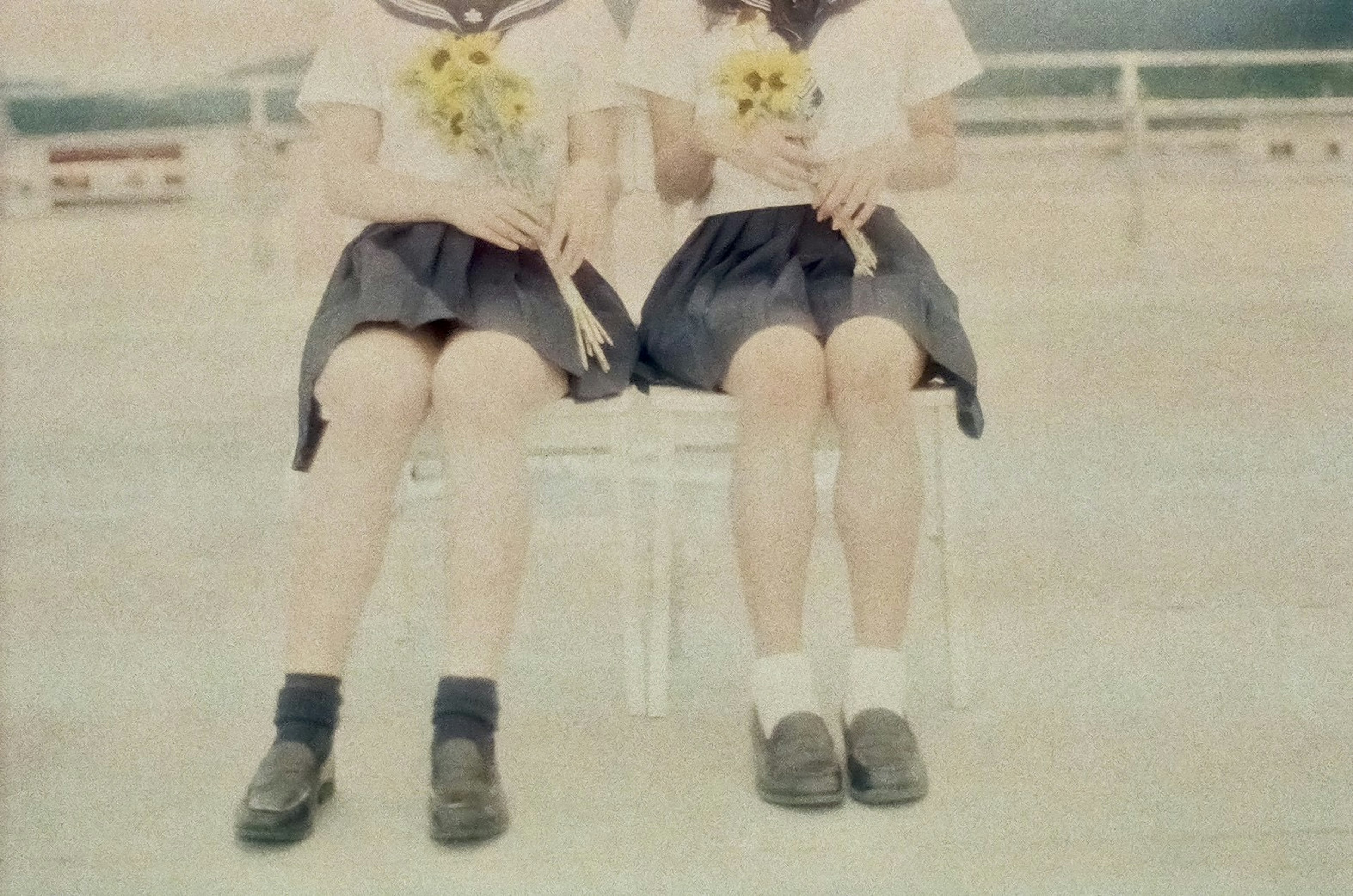 Two girls sitting on a chair holding sunflowers