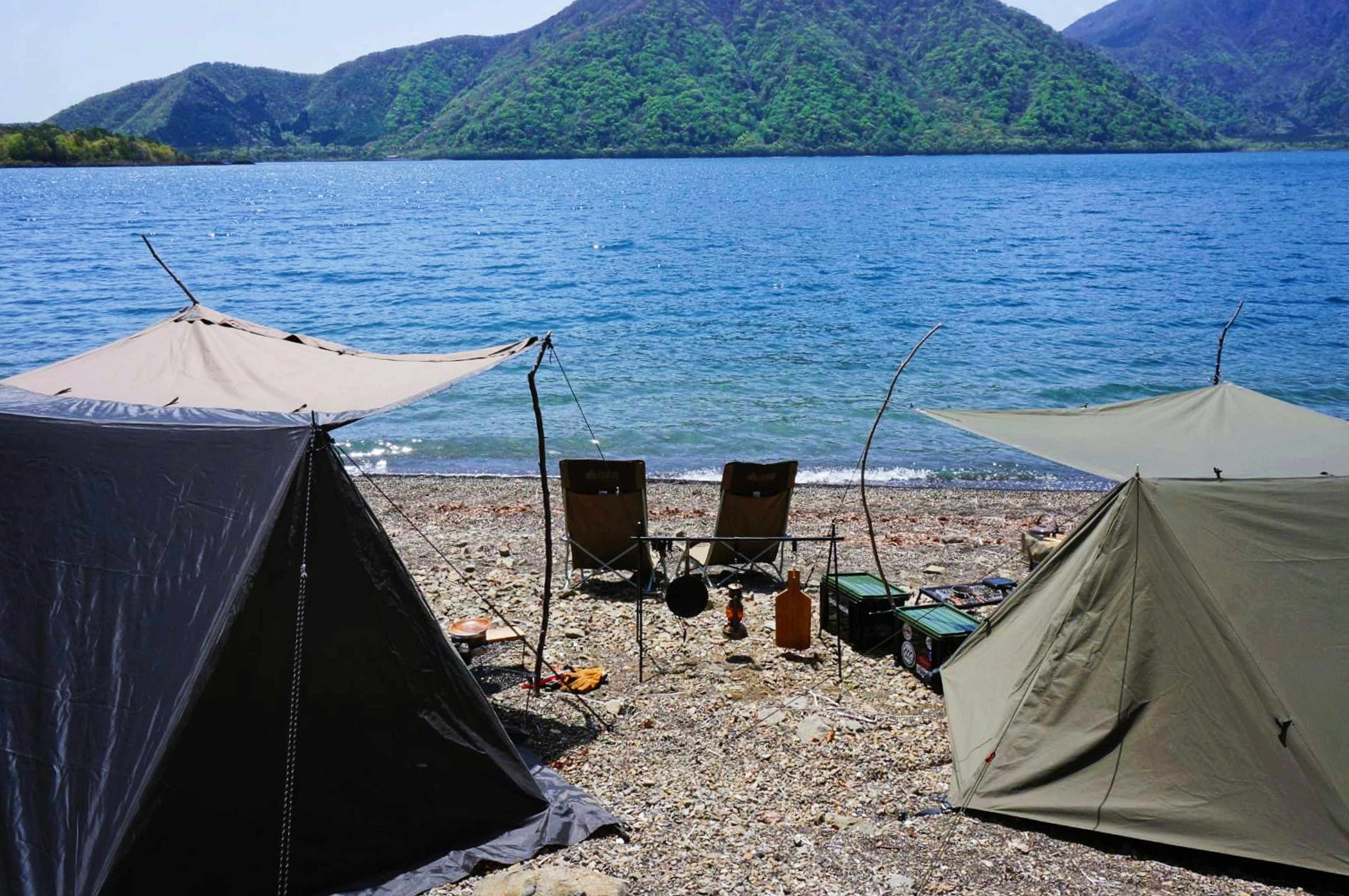 湖の近くにテントと椅子が並ぶキャンプサイトの風景