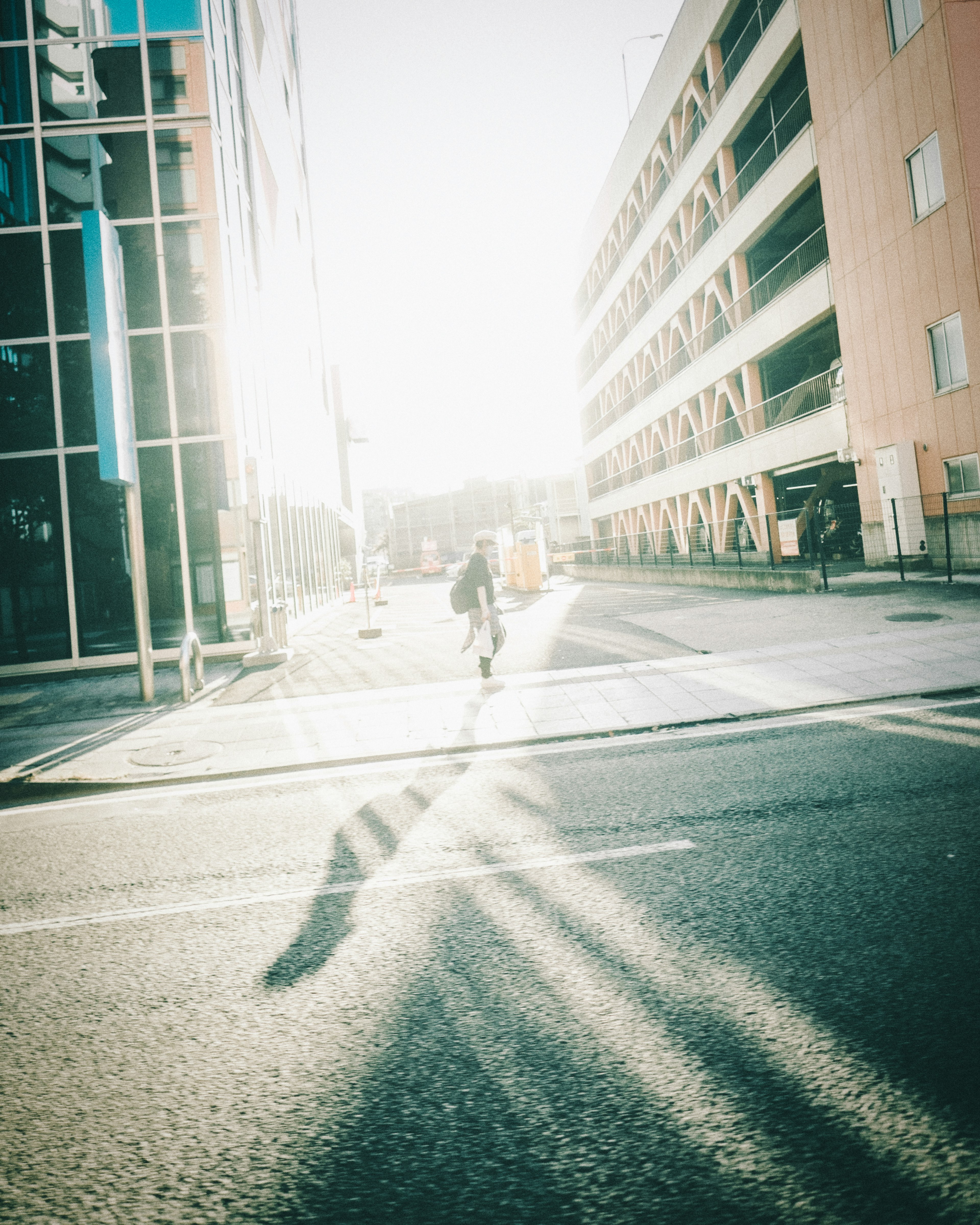 Eine Person, die im hellen Sonnenlicht geht und lange Schatten auf die Straße wirft