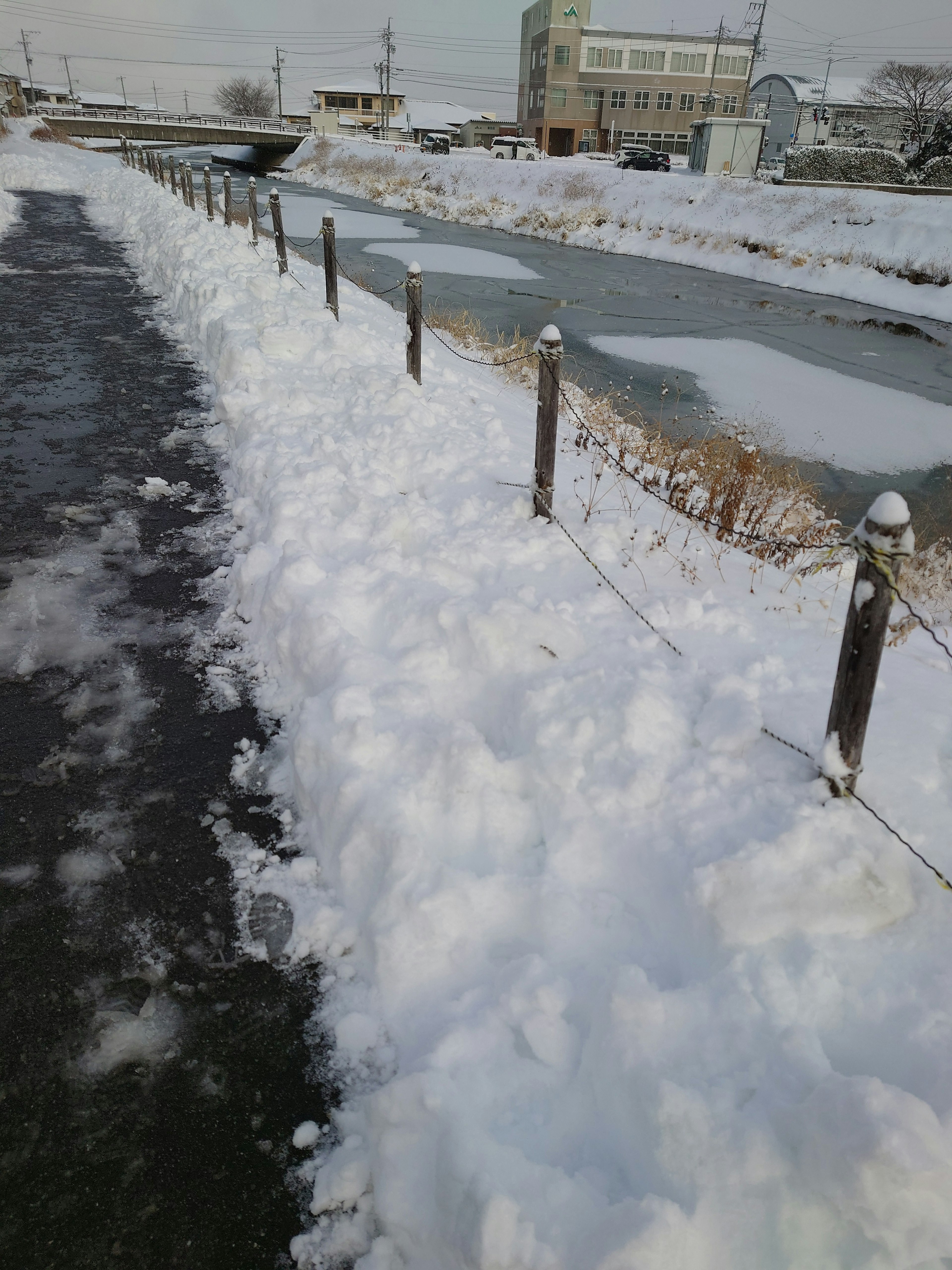 Snow-covered riverside path with a fence