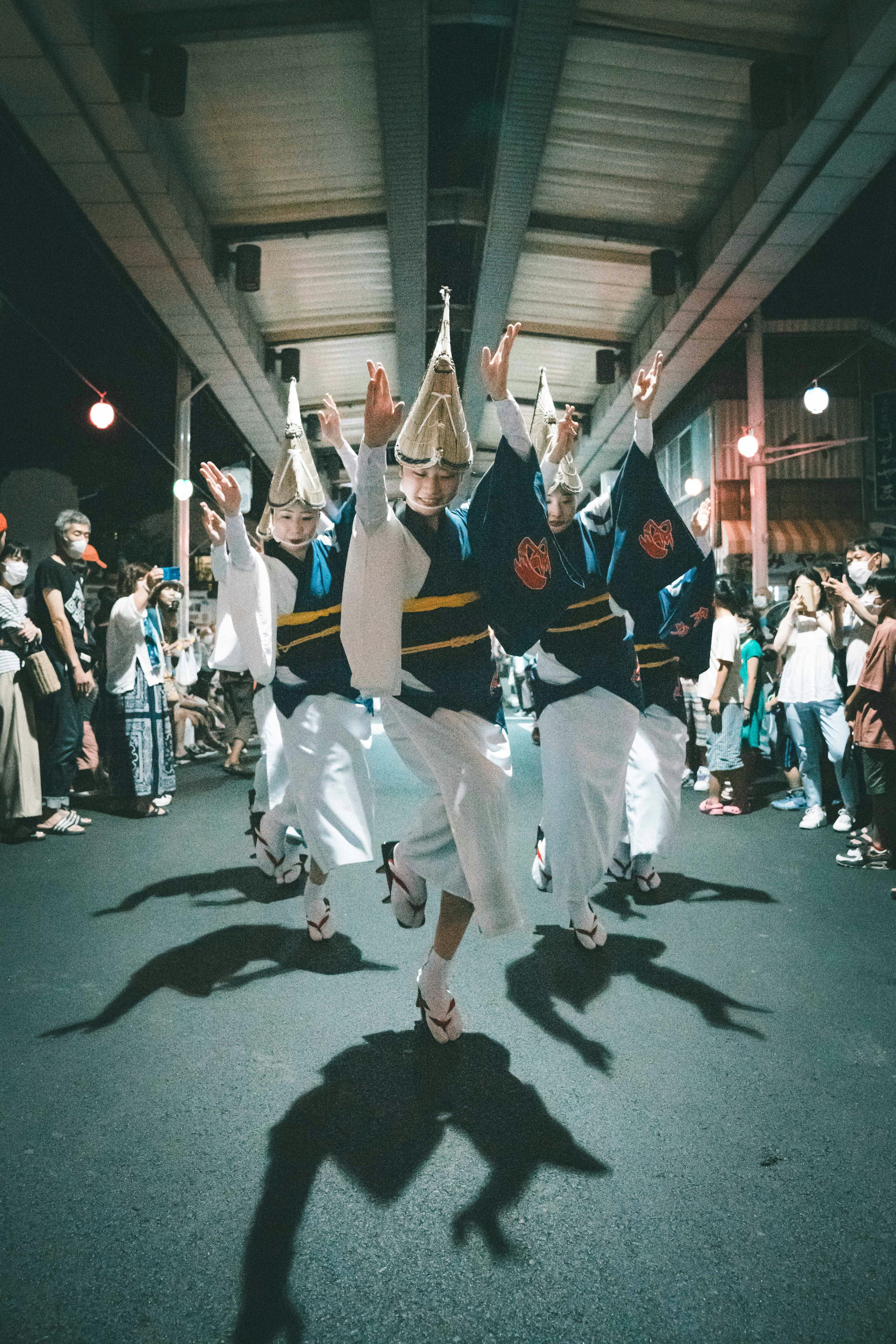 Grupo de bailarines actuando en un festival nocturno vistiendo trajes tradicionales con sombras proyectadas en el suelo