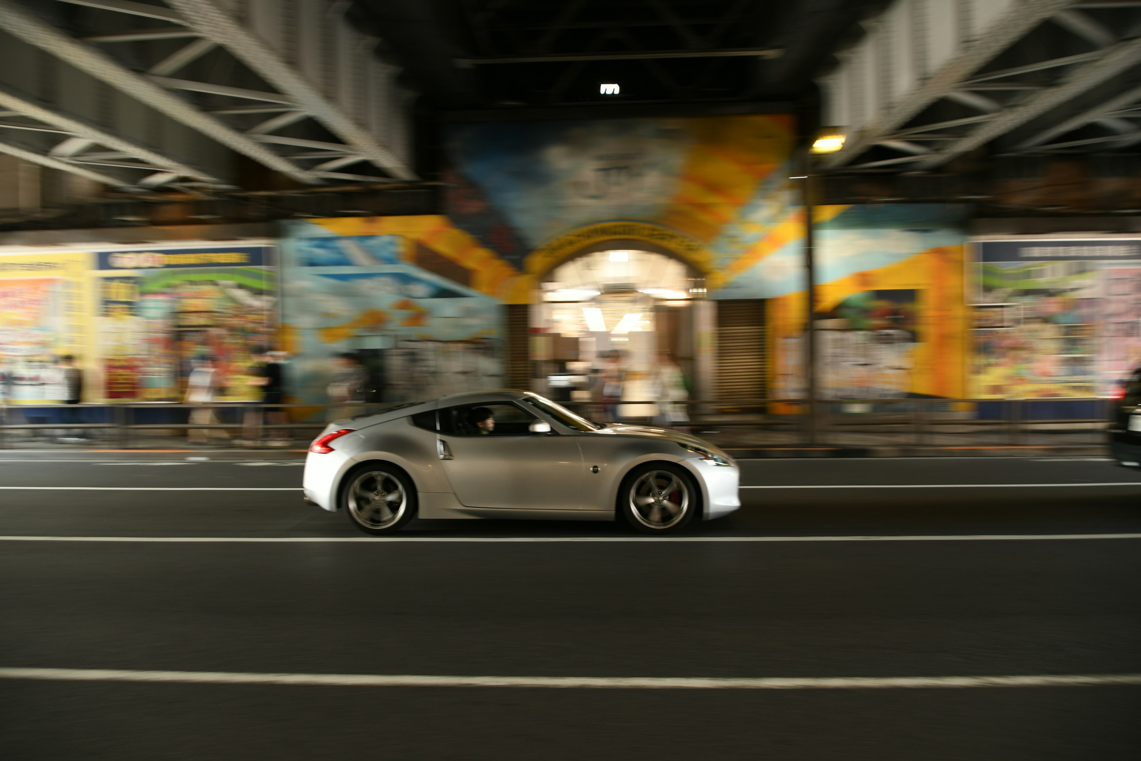 Auto sportiva argento in movimento con murales colorati in un contesto urbano