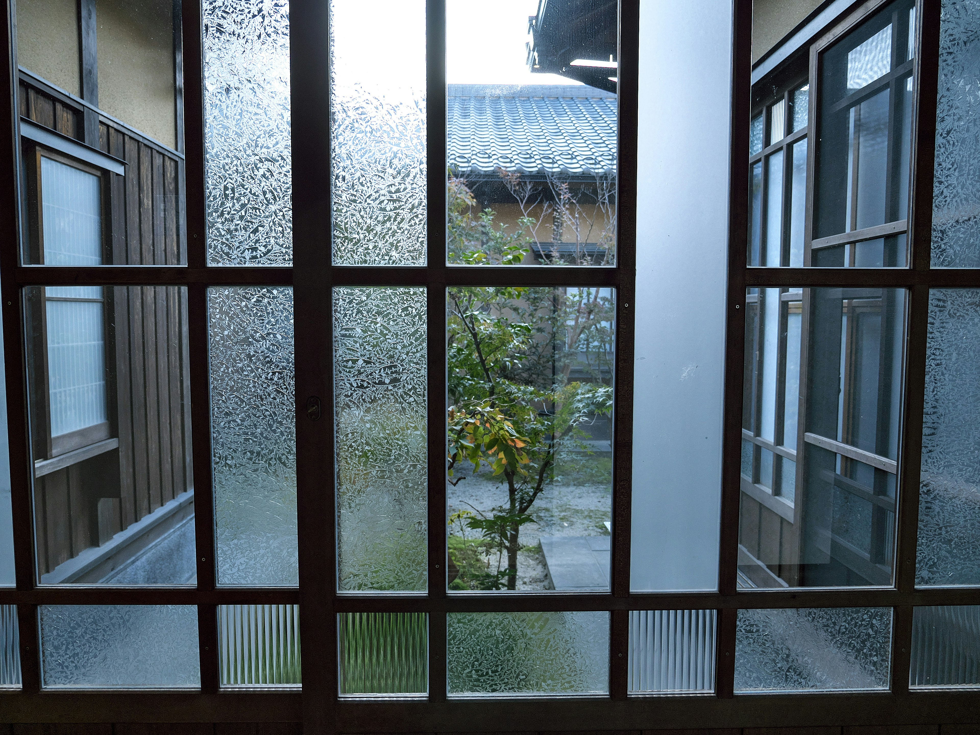 Blick auf einen Garten durch ein beschlagenes Fenster in einem traditionellen japanischen Gebäude