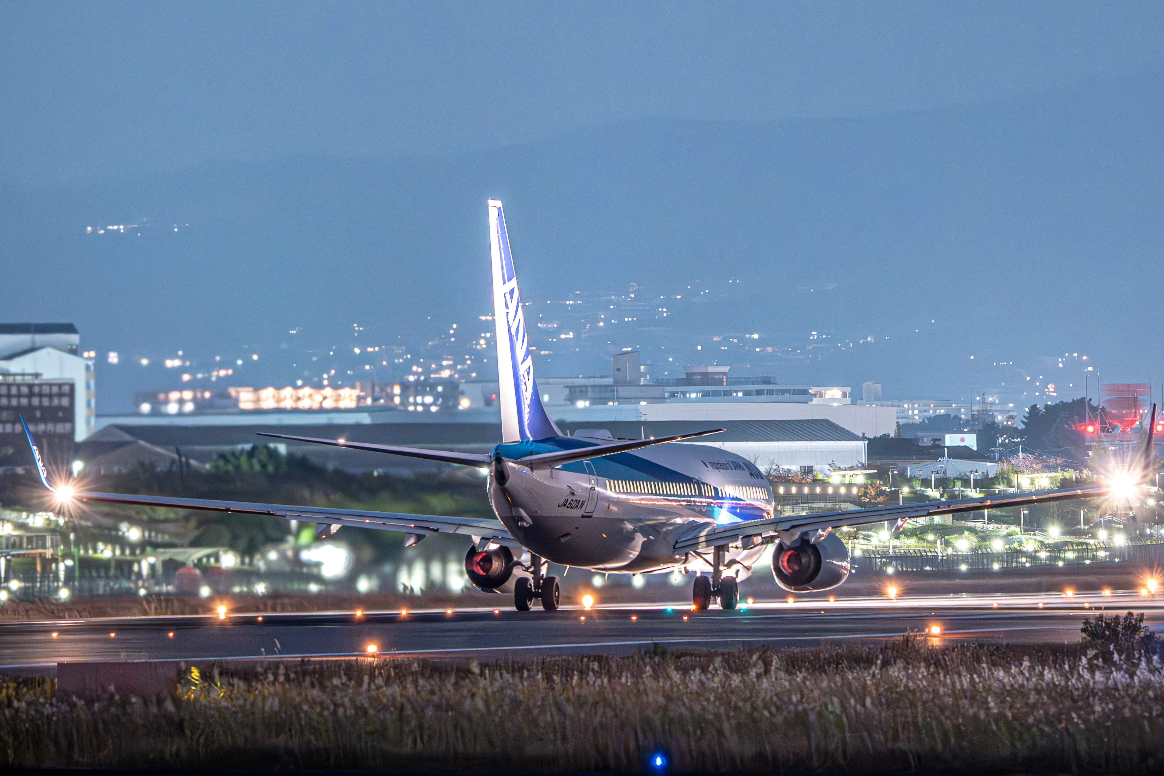 Passenger aircraft taxiing on runway at night with city lights in the background