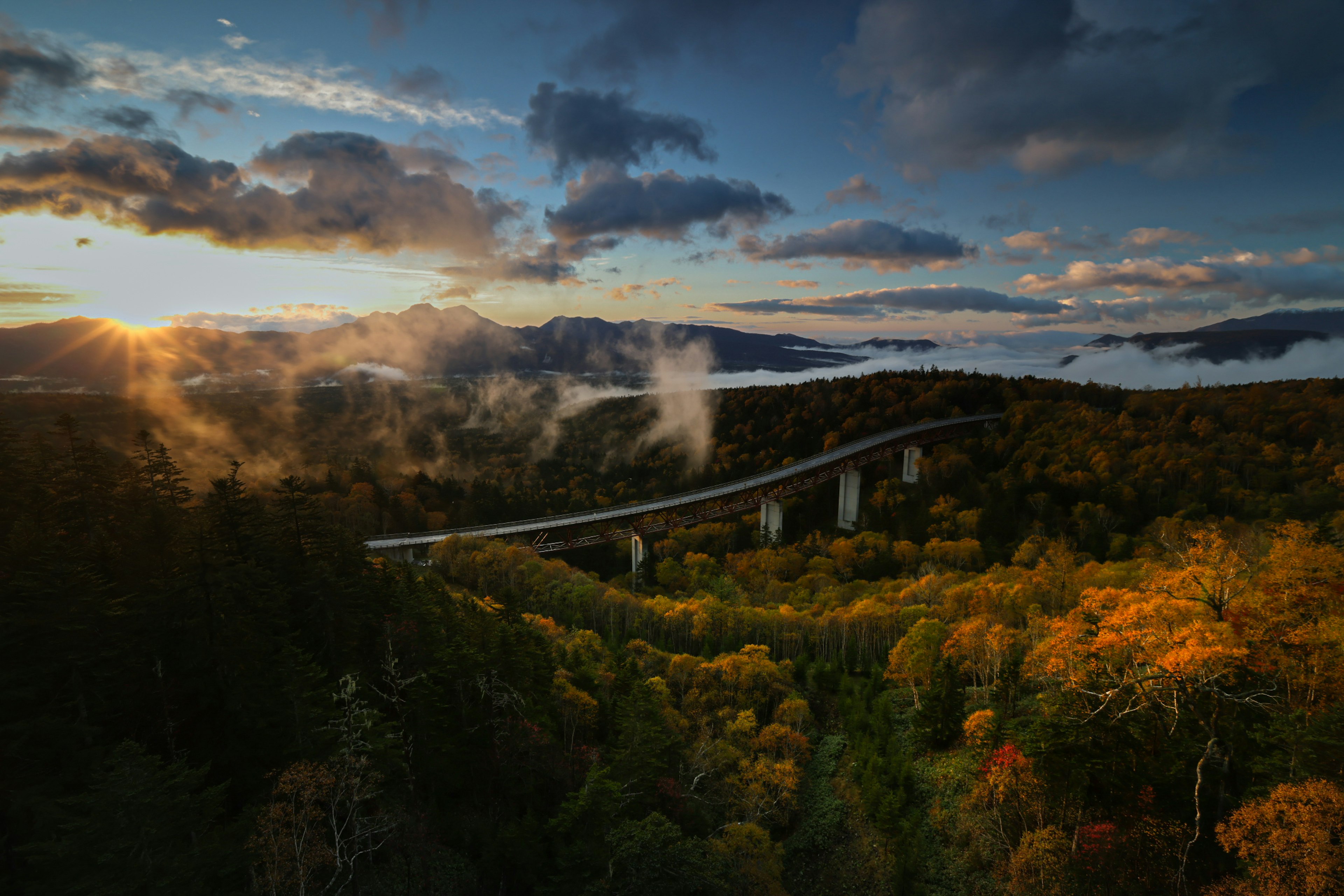 Malersicher Blick auf eine Brücke über Berge mit Sonnenuntergang und buntem Laub