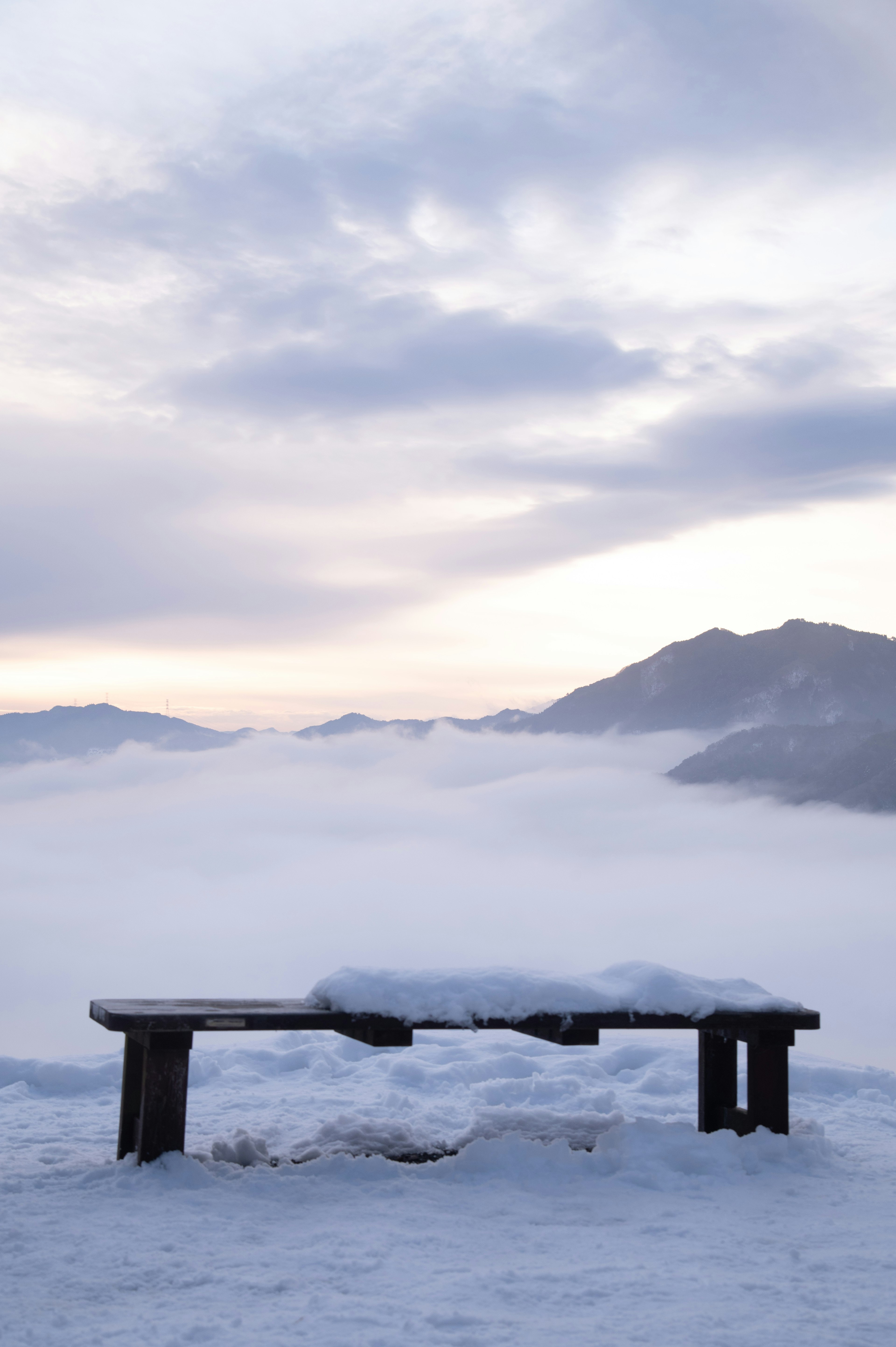 Snow-covered bench overlooking misty mountains at dawn