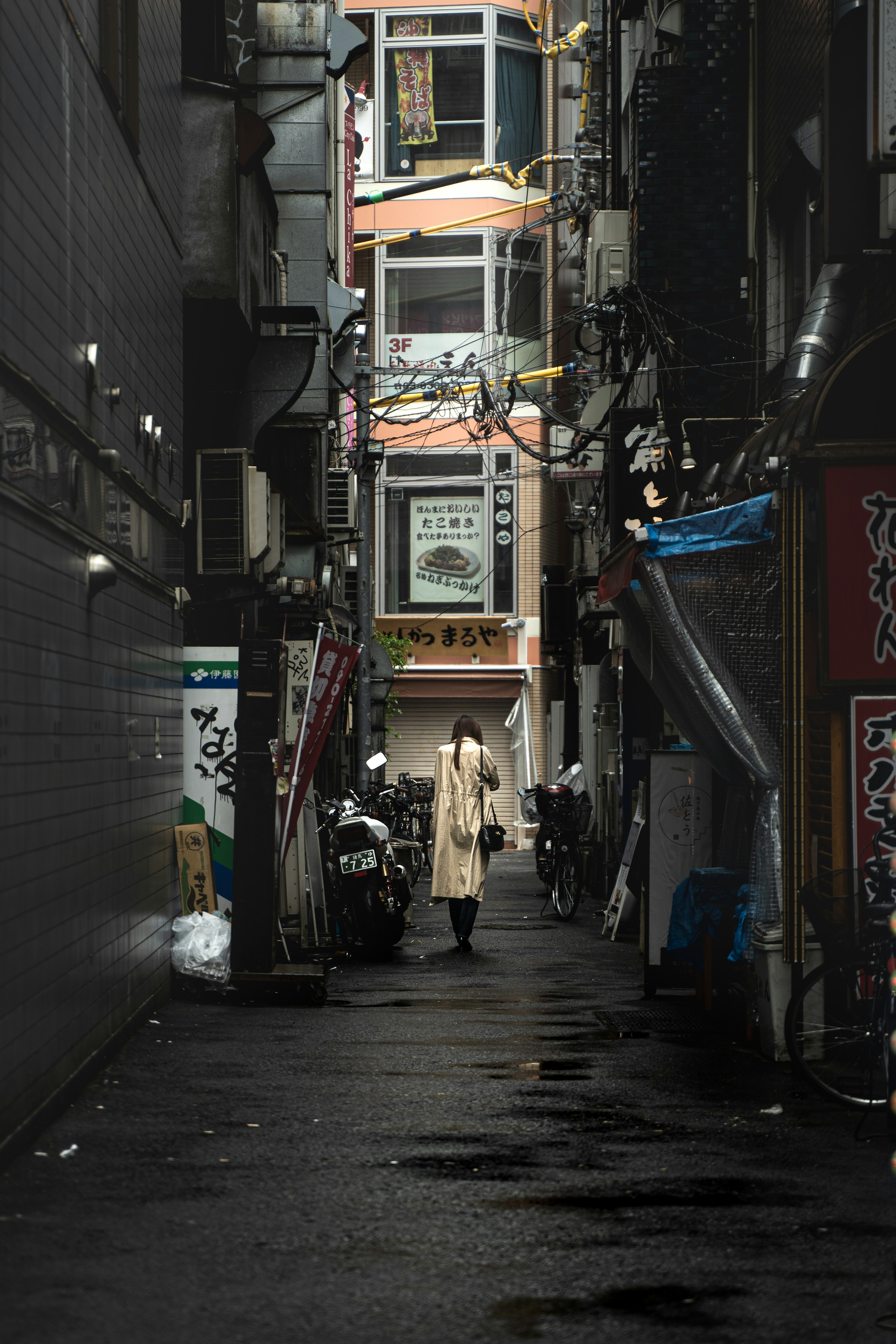 Person in white coat standing in narrow alley with buildings in background