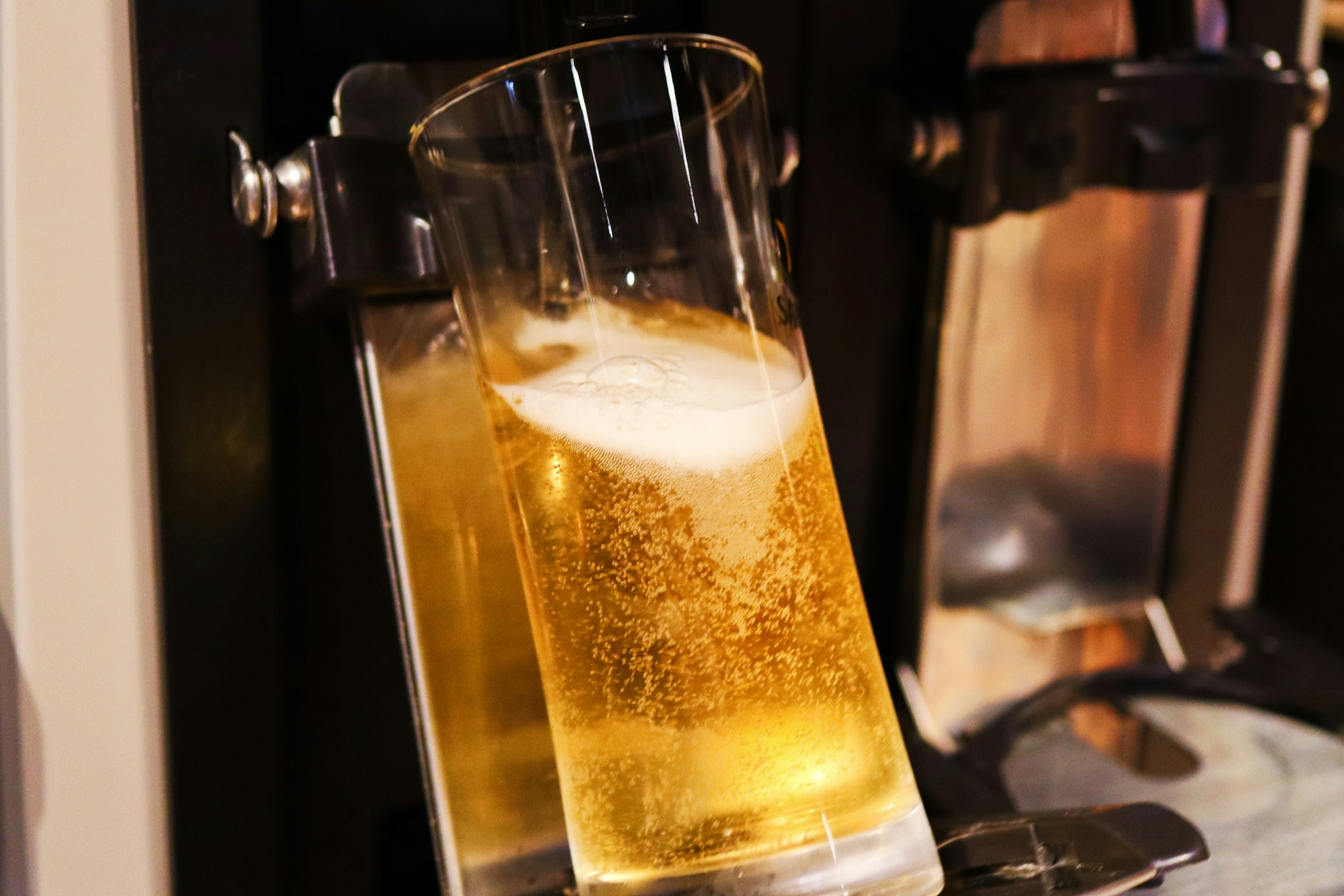 A glass of beer filled with golden liquid and foam on top placed on a beer dispenser