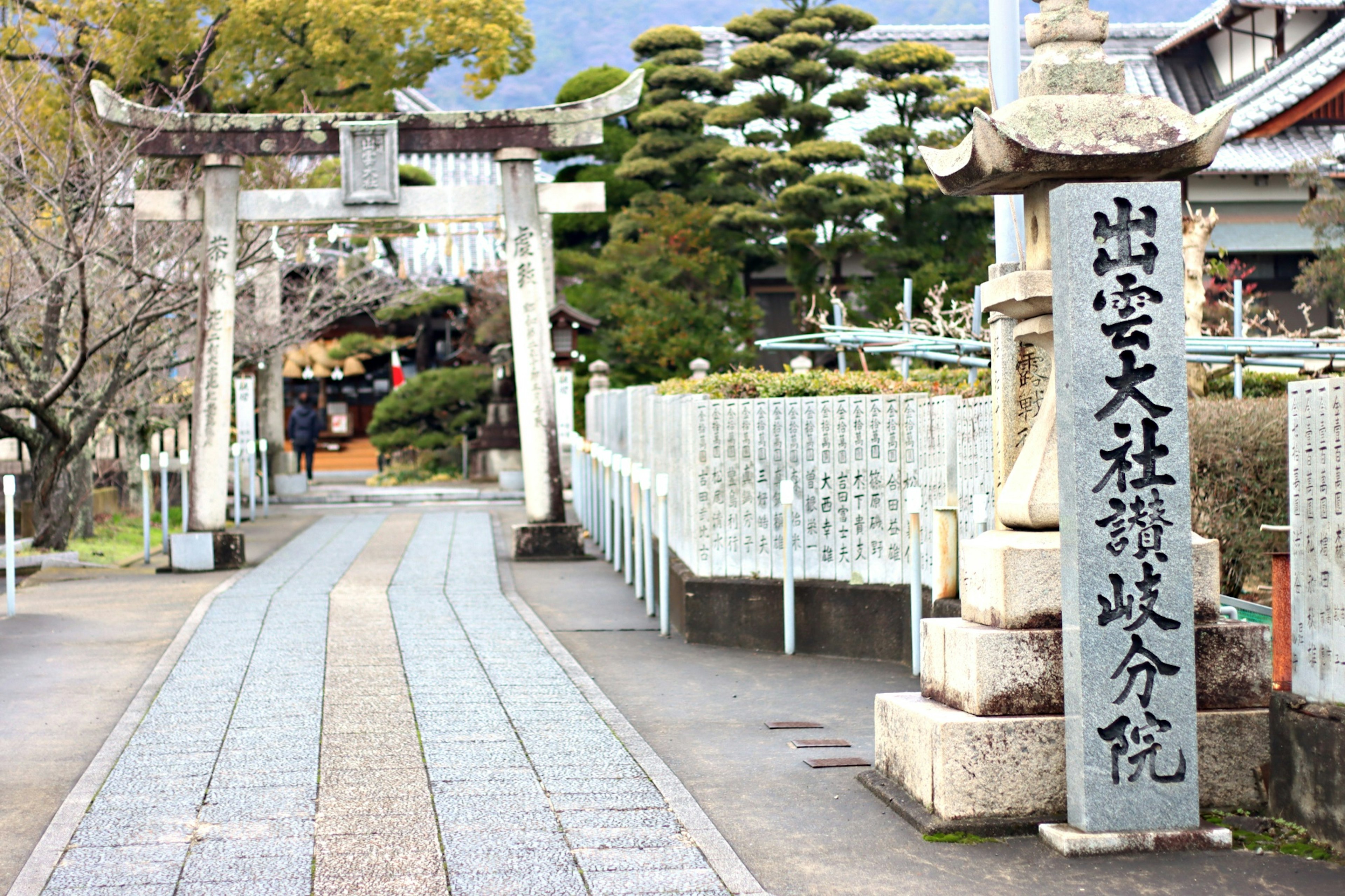 Con đường dẫn đến Izumo Taisha với cổng torii bằng đá và đài tưởng niệm cây cối xanh tươi và núi non ở phông nền