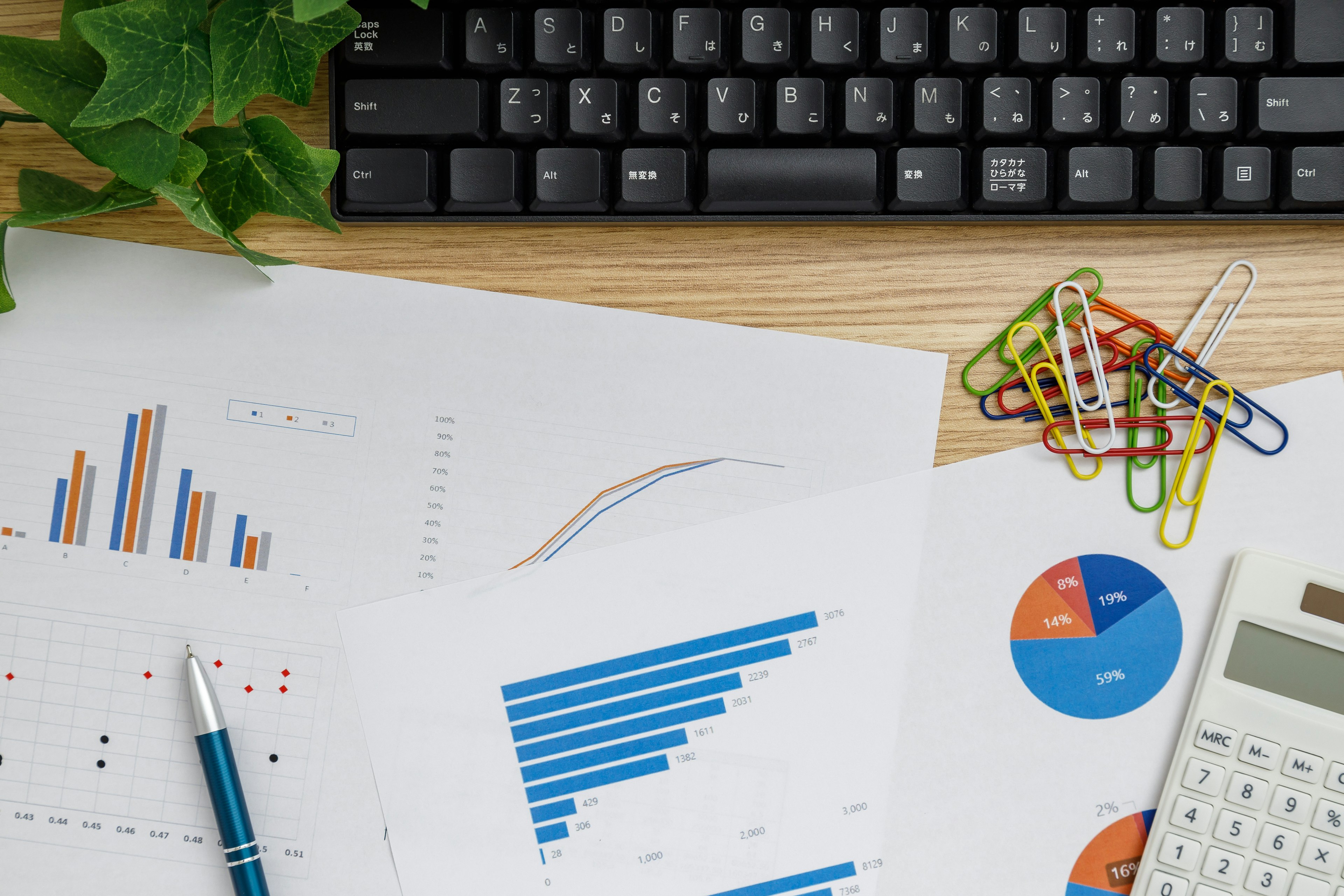 Desk with printed charts and graphs calculator pen keyboard and paper clips arranged neatly