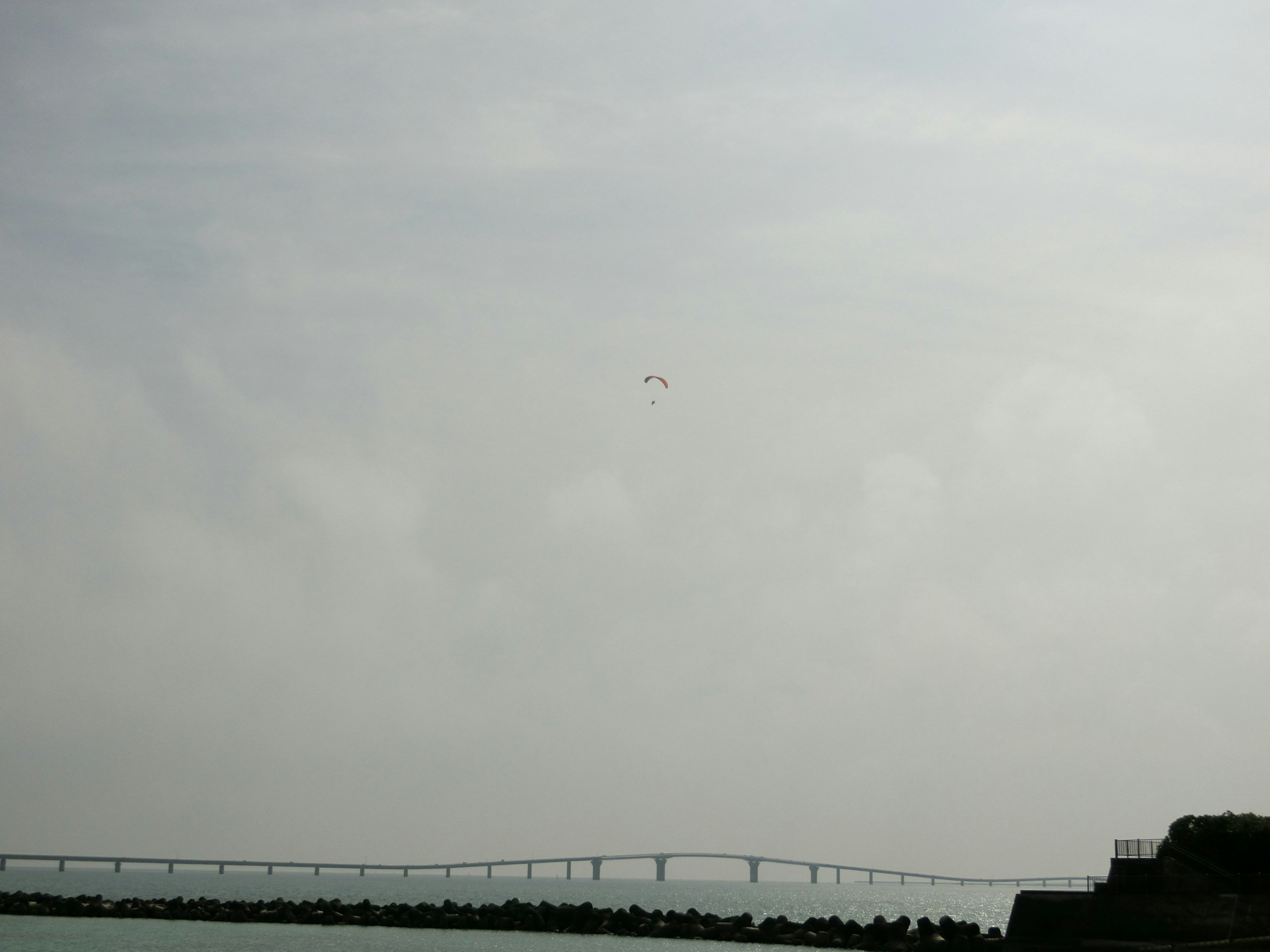 Puente bajo un cielo nublado con un objeto volador a lo lejos