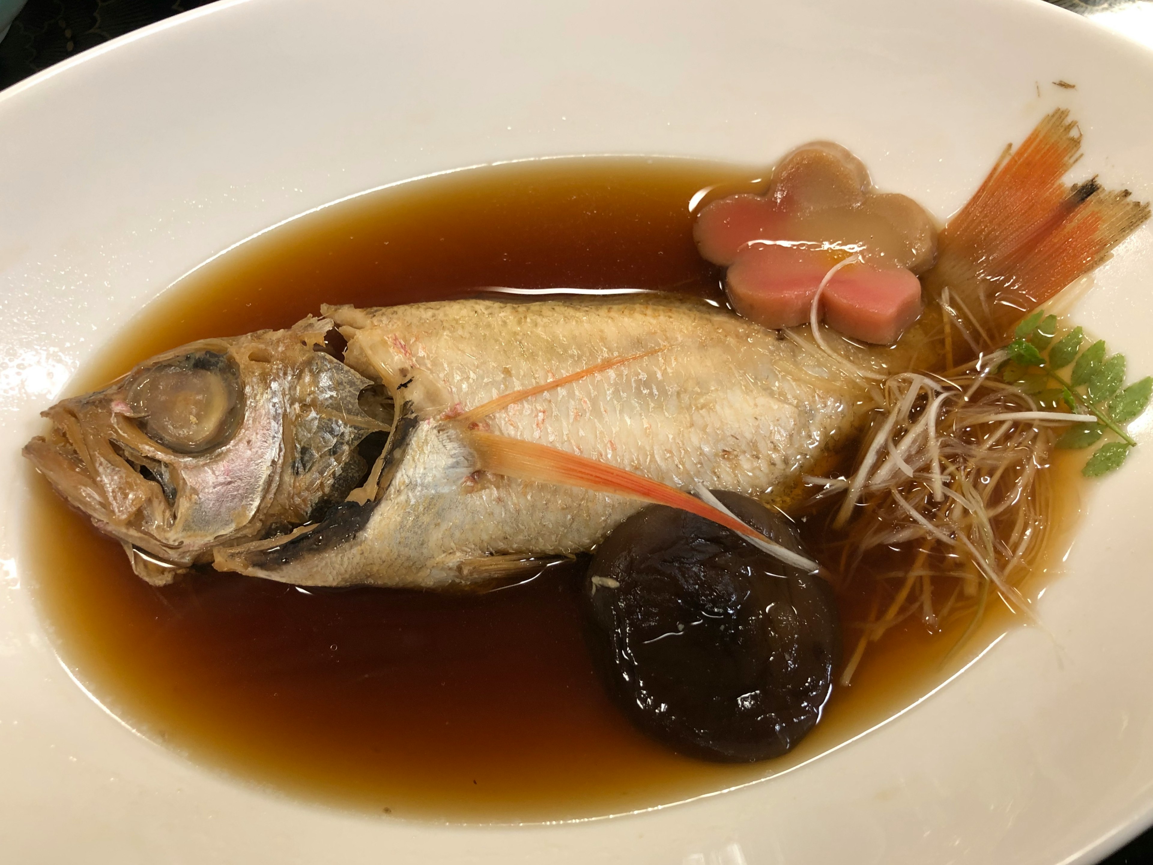 煮込まれた魚の料理に黒い干し椎茸と生姜のトッピングがある