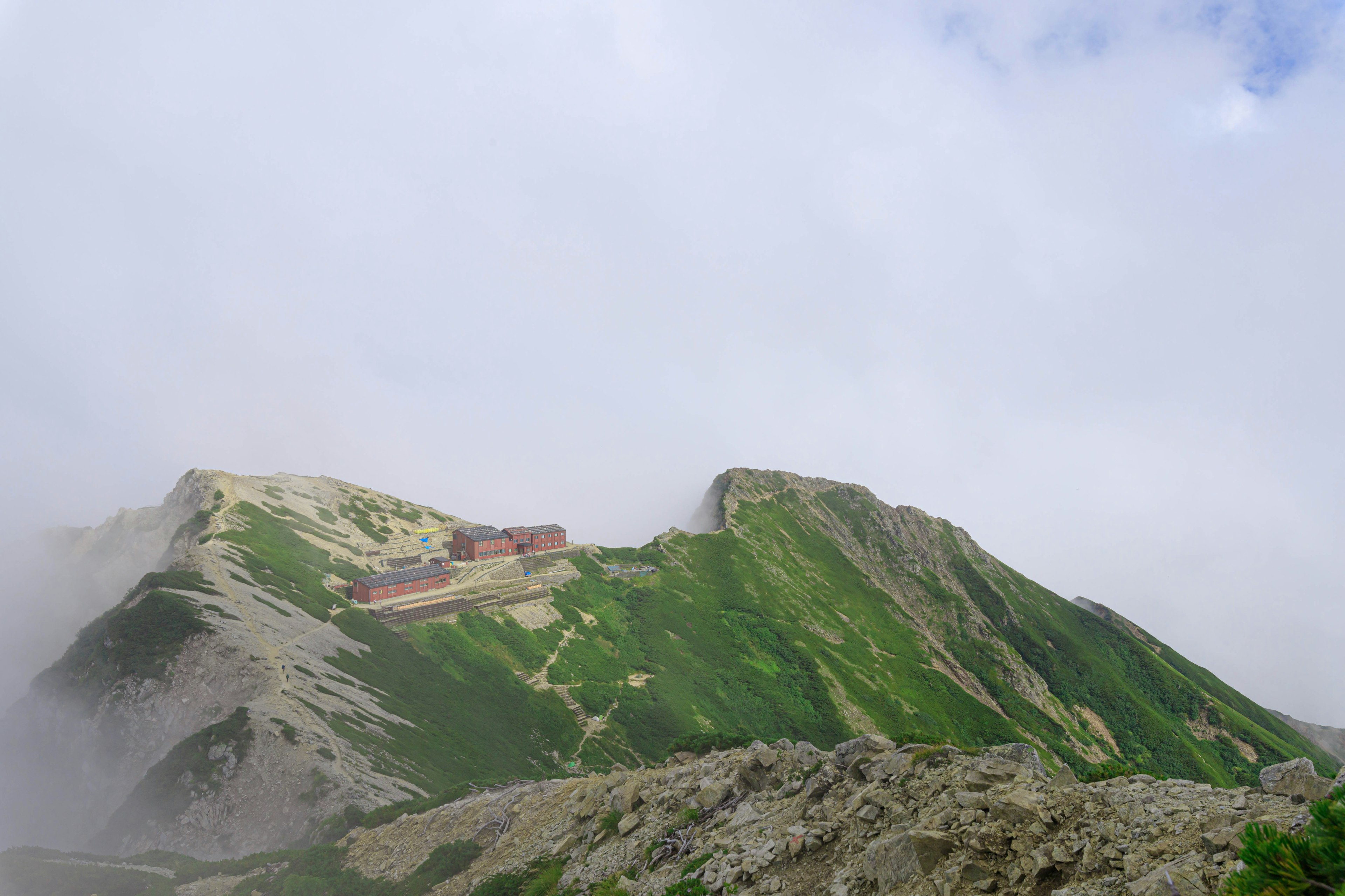 Paisaje montañoso envuelto en niebla con laderas verdes y un edificio rojo distintivo