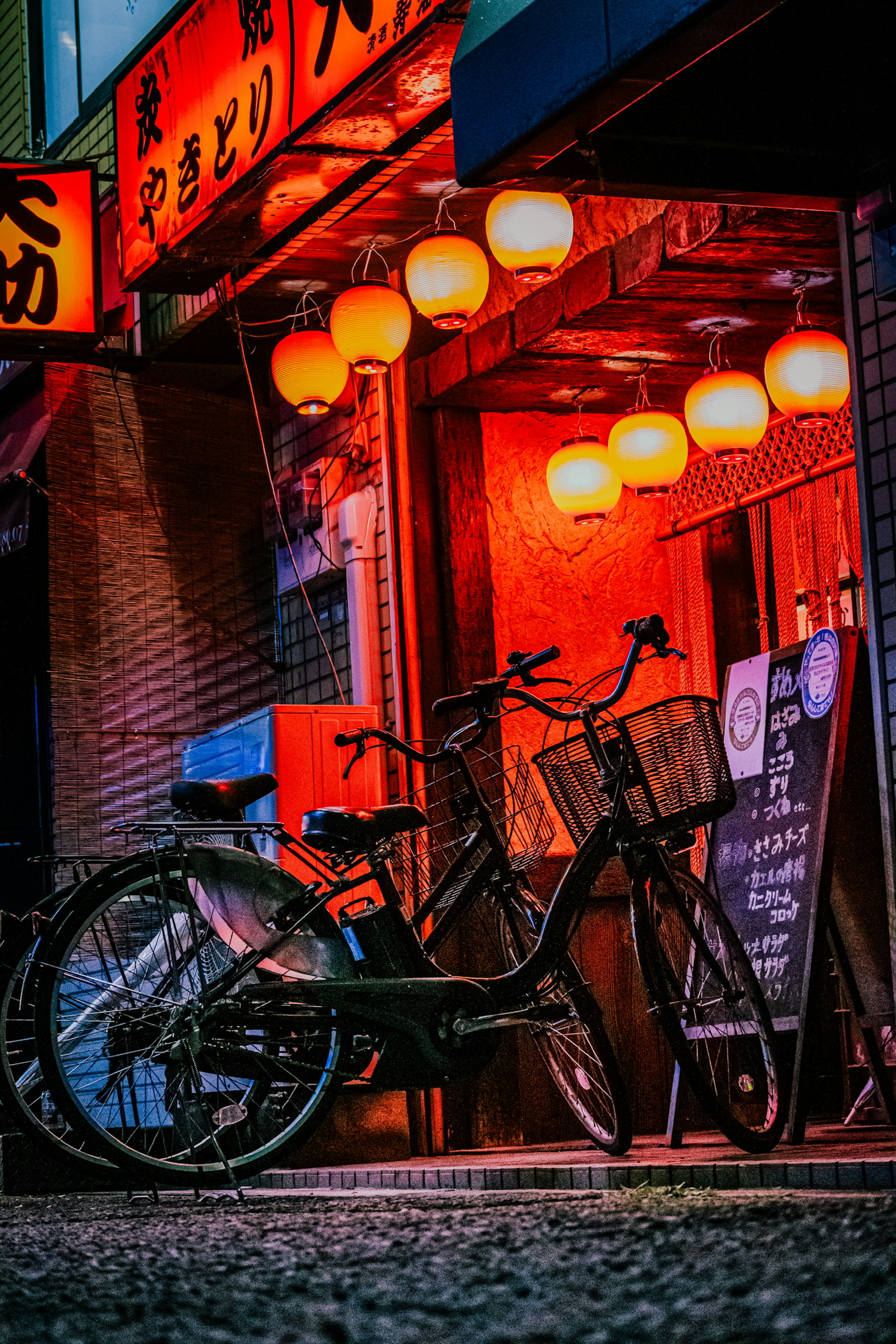 Bicicletta sotto lanterne rosse luminose all'esterno di un izakaya giapponese