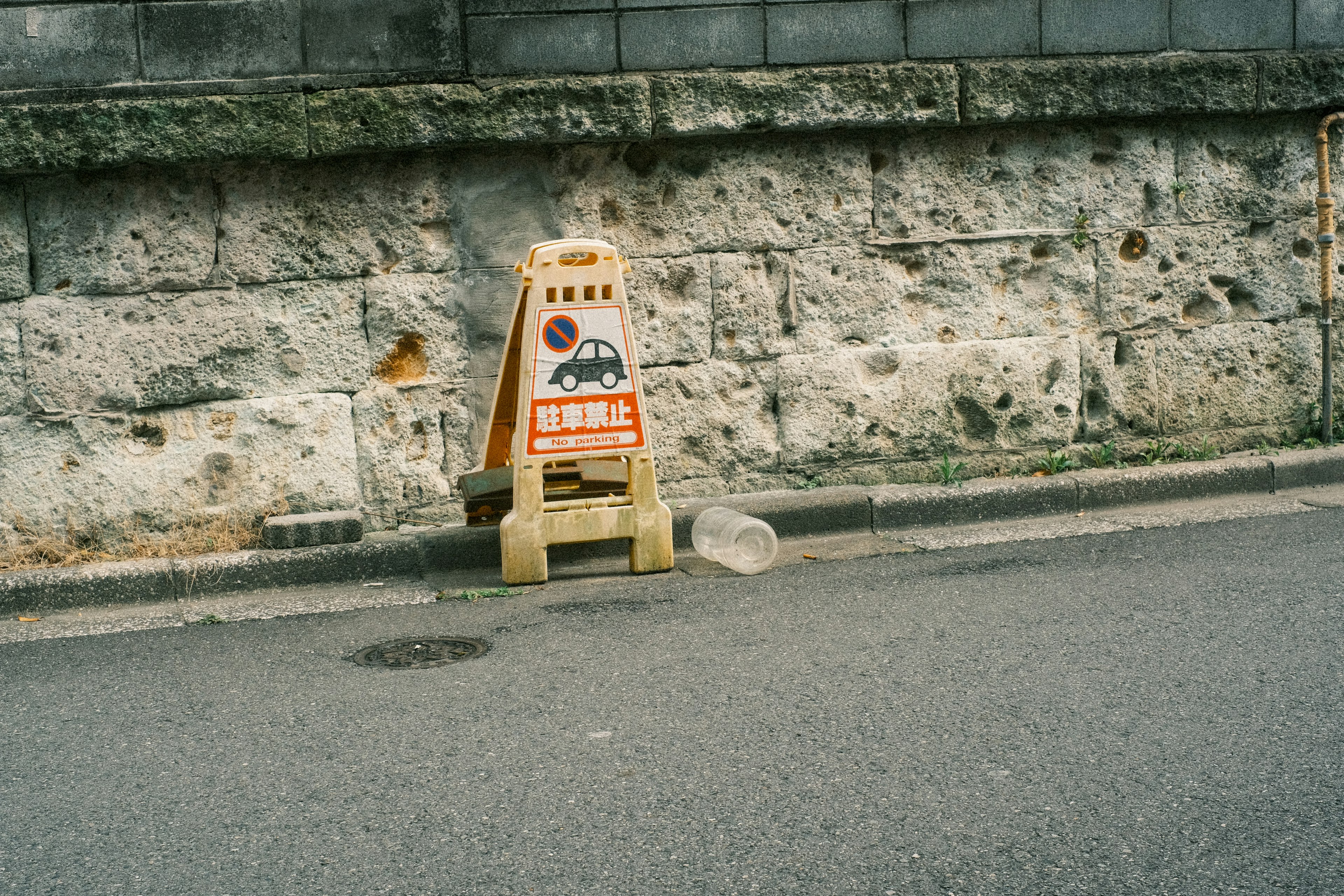 Wooden warning sign next to a textured stone wall on the street