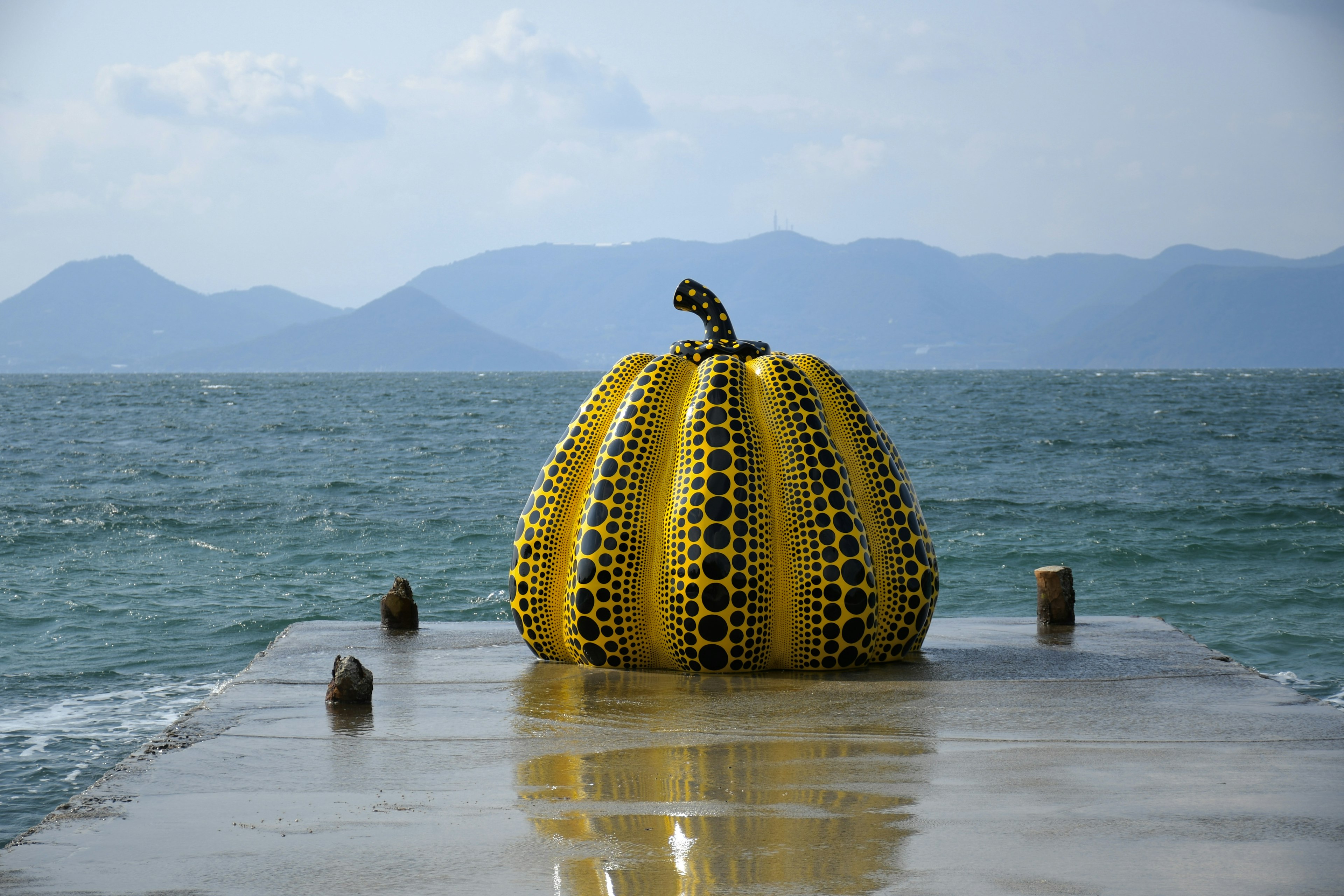 Escultura de calabaza amarilla en un muelle con océano y montañas al fondo