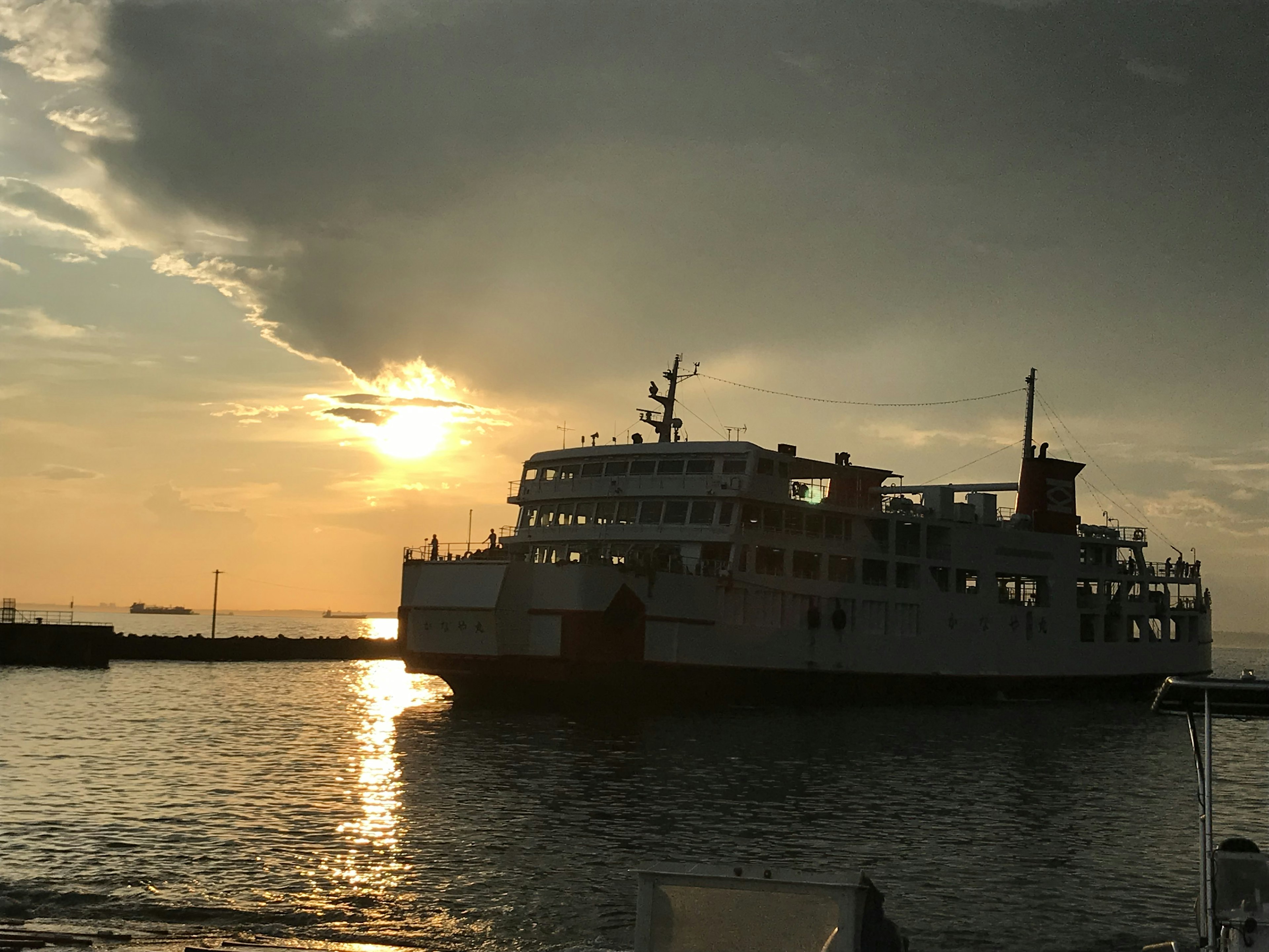 Eine Fähre, die gegen einen Sonnenuntergang über ruhigem Wasser silhouettiert ist