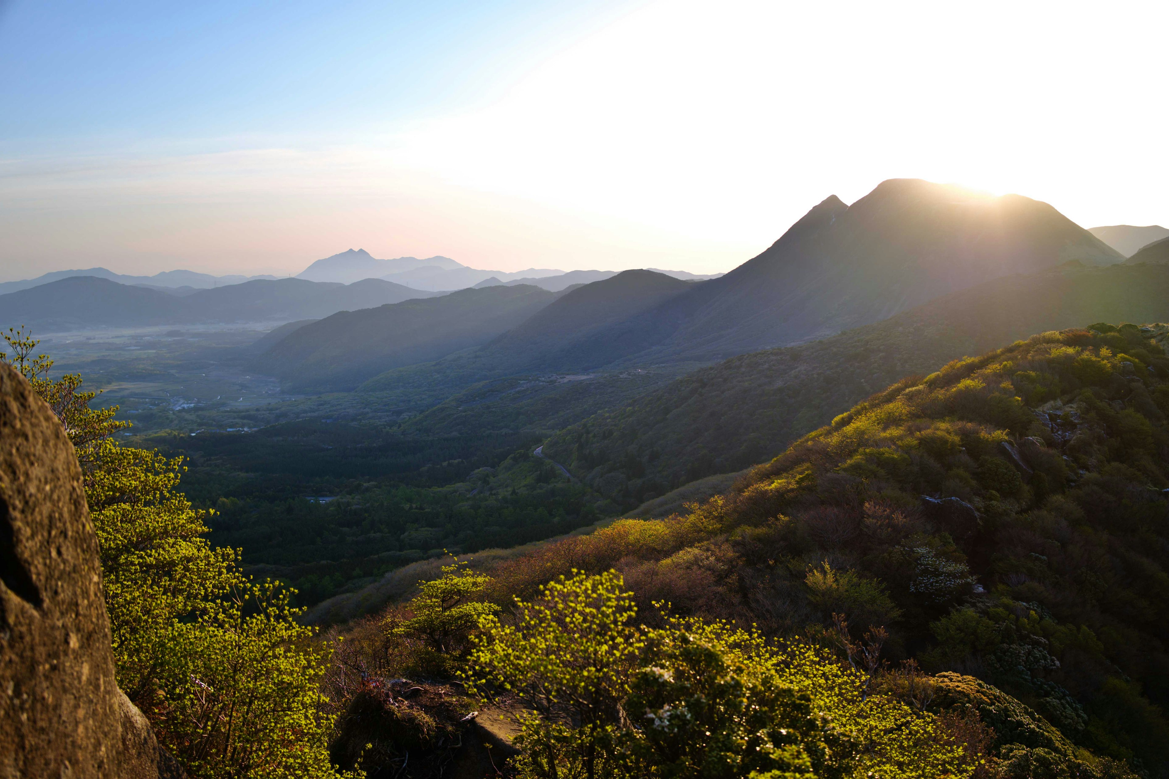 ทิวทัศน์ของภูเขาพร้อมกับพระอาทิตย์ตกที่สว่างไสวและพืชพรรณเขียวชอุ่ม