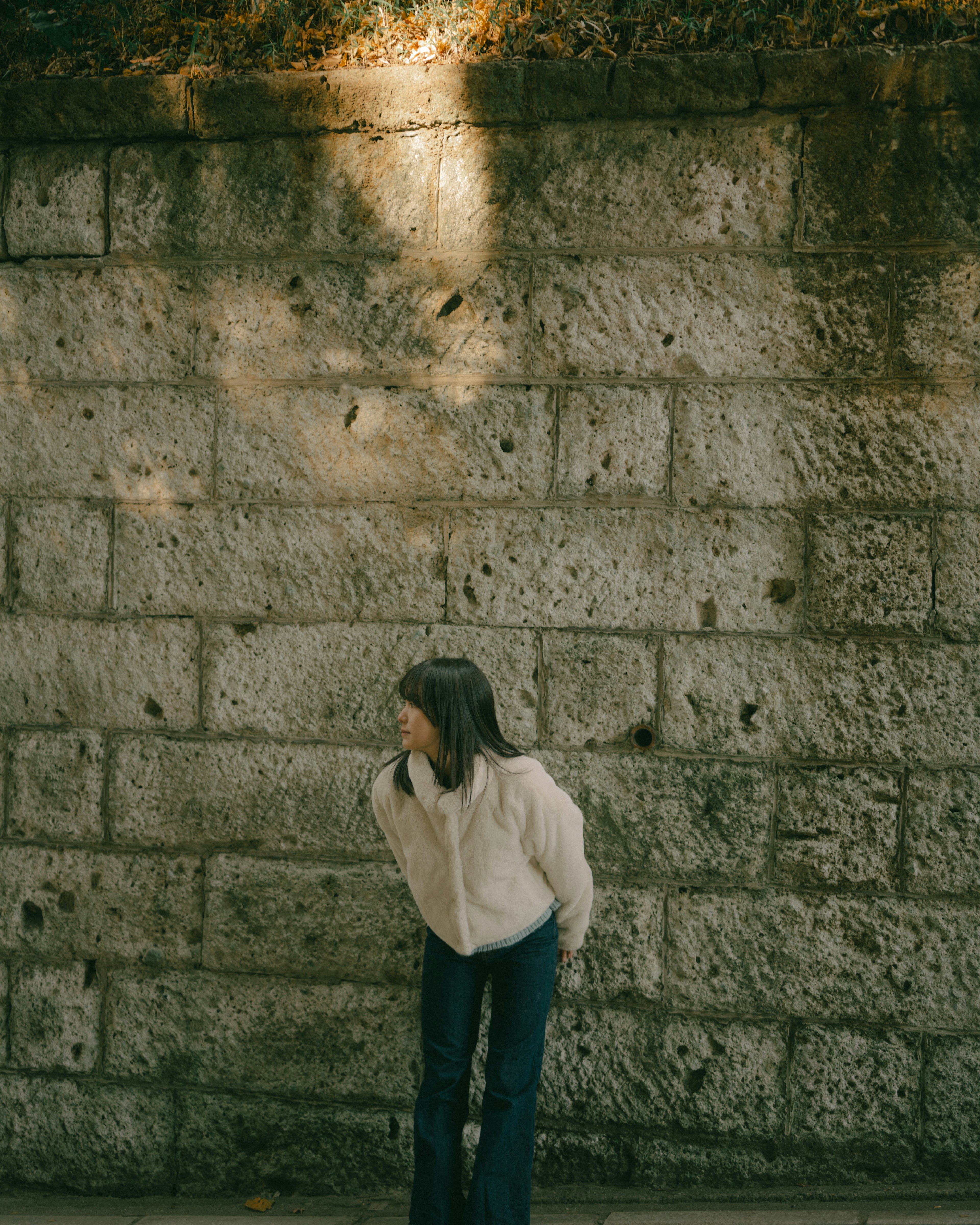 A girl standing in front of a stone wall with soft light illuminating her