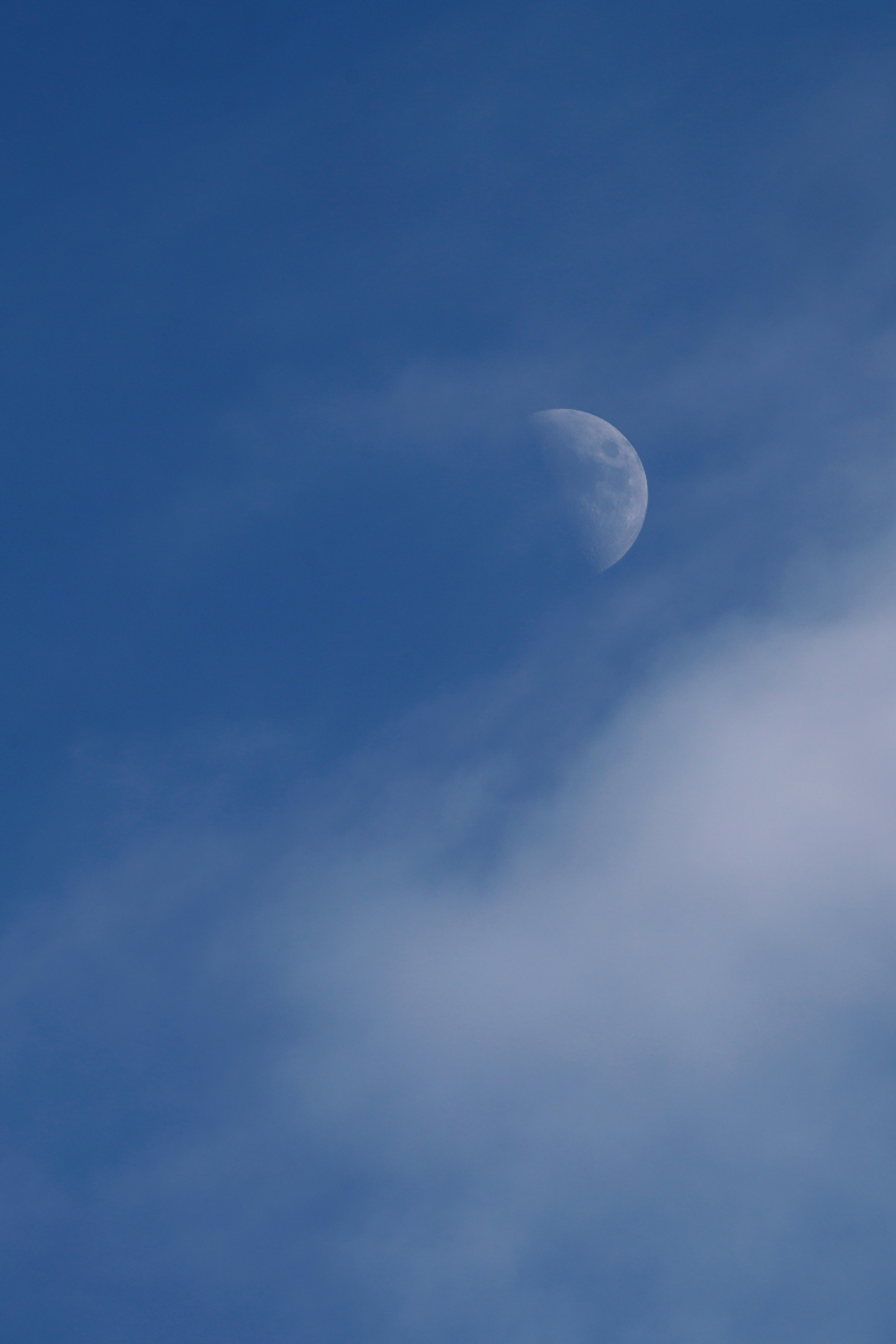 Luna creciente visible en un cielo azul con nubes