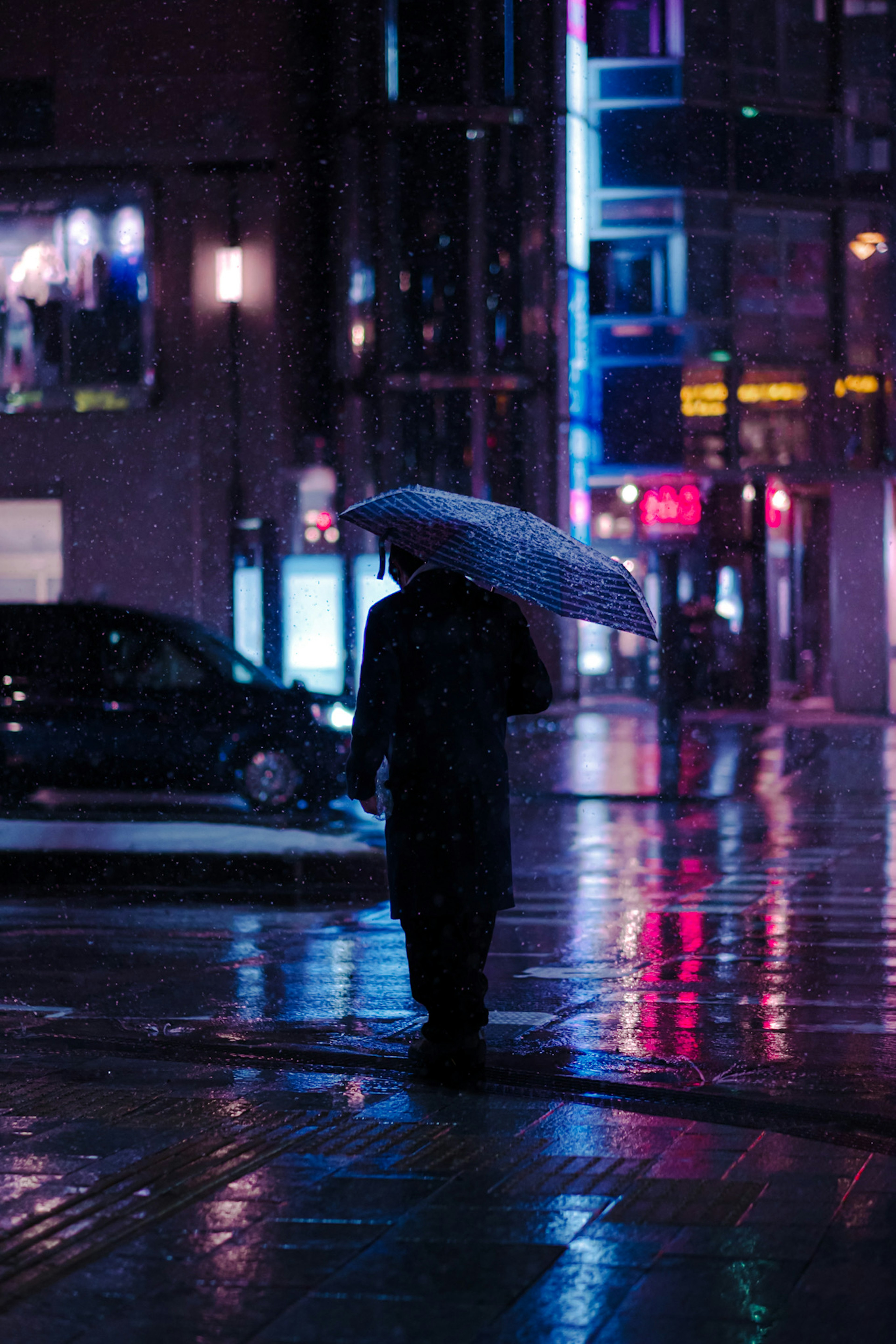 雨の中、傘を持って歩く人物のシルエット 夜の都市のネオンライトが反射している