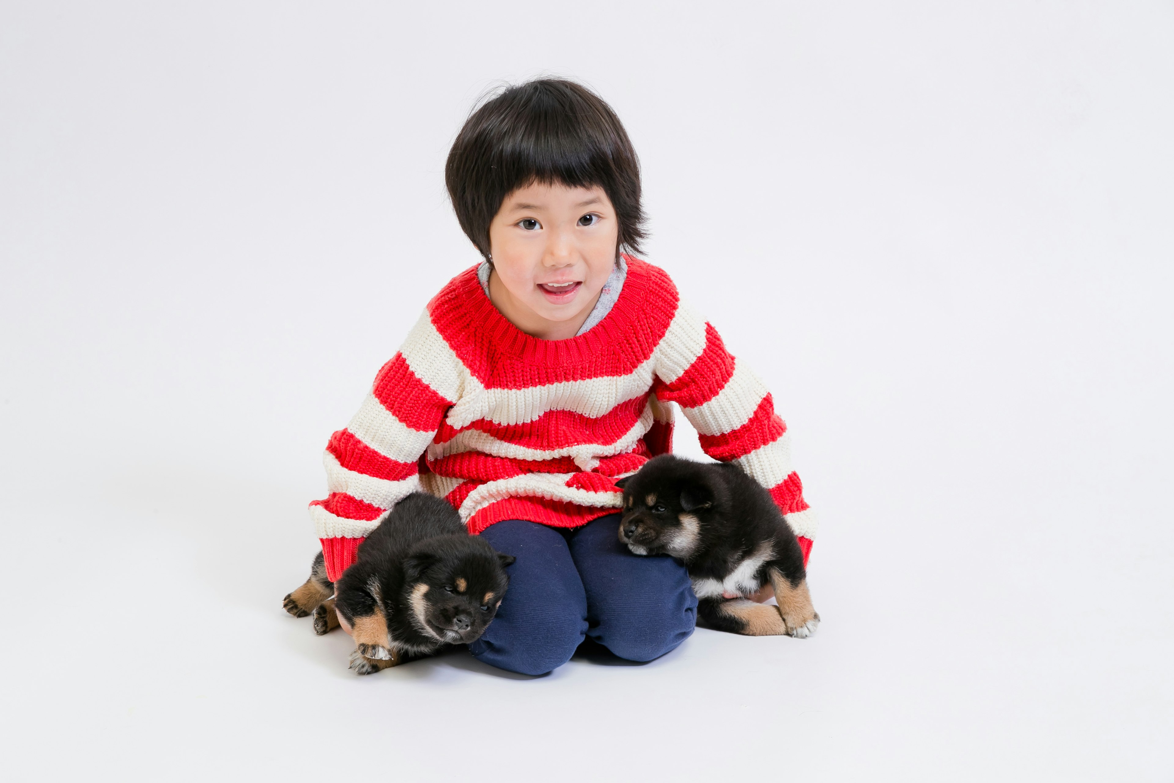 Bambino in maglione a righe rosse e bianche seduto con due cuccioli