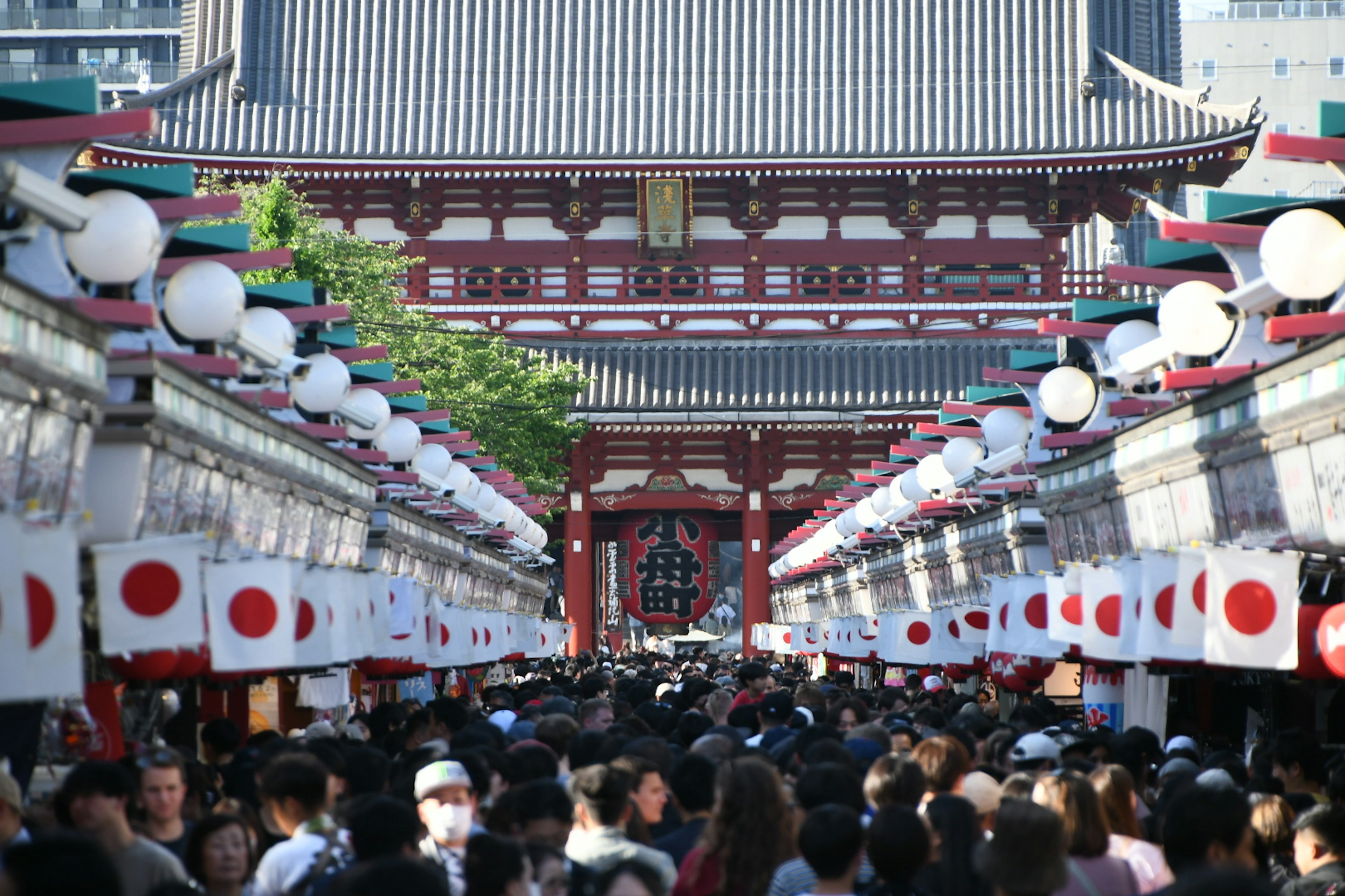 Jalan yang ramai dengan bendera Jepang dan gerbang Kuil Senso-ji terlihat