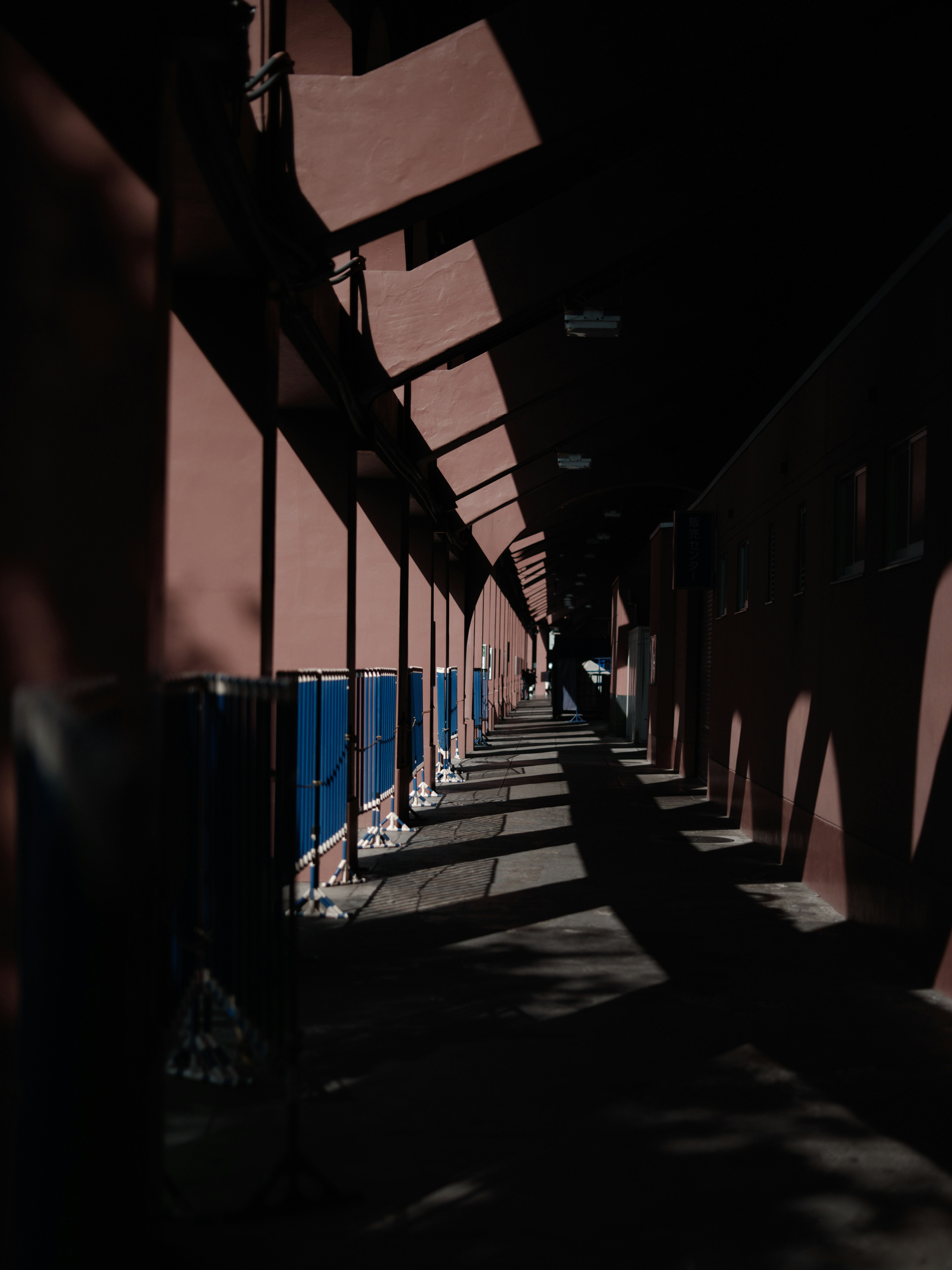 Un long couloir avec des murs rouges et des panneaux bleus projetant des ombres