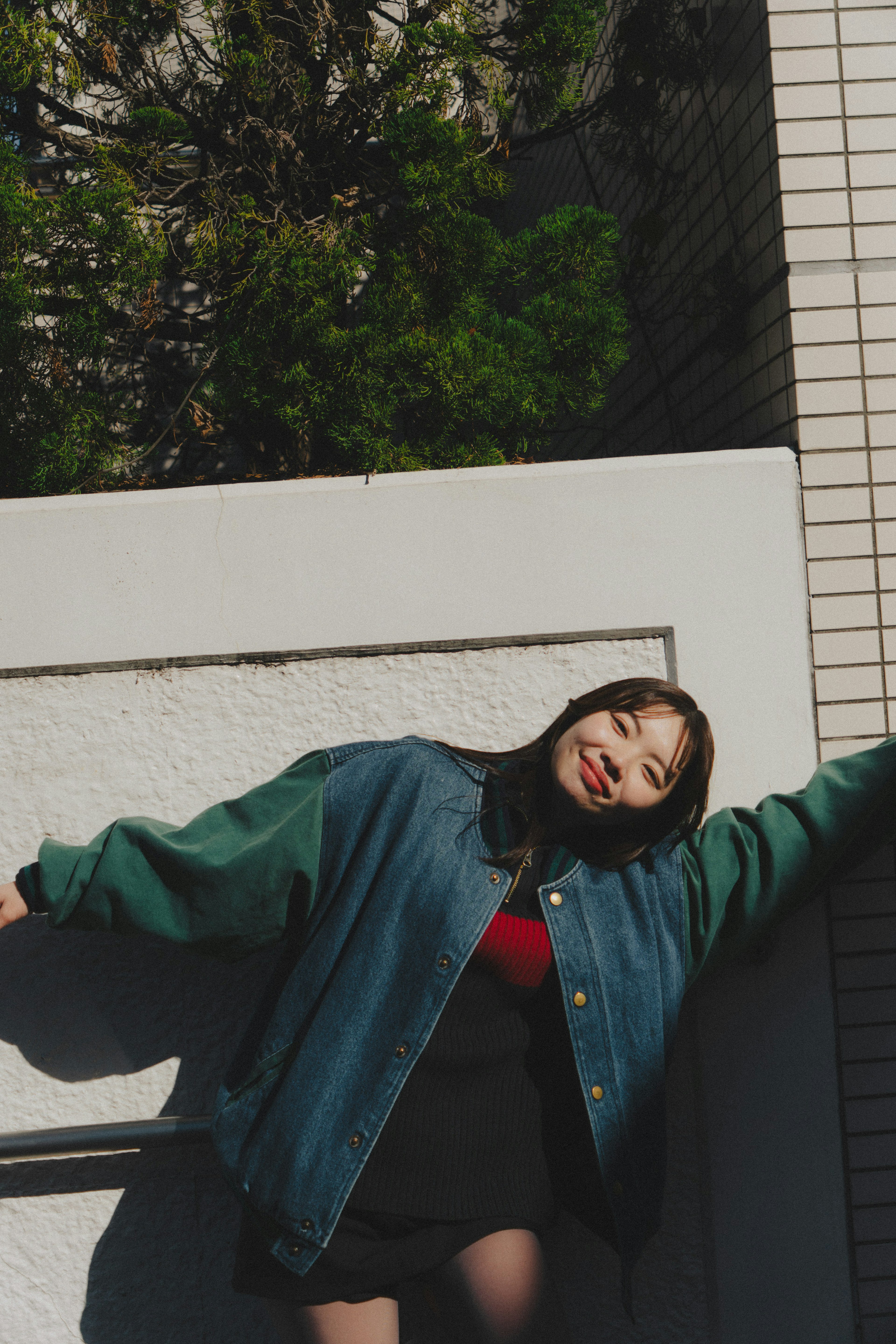 A woman wearing a teal jacket leaning against a wall