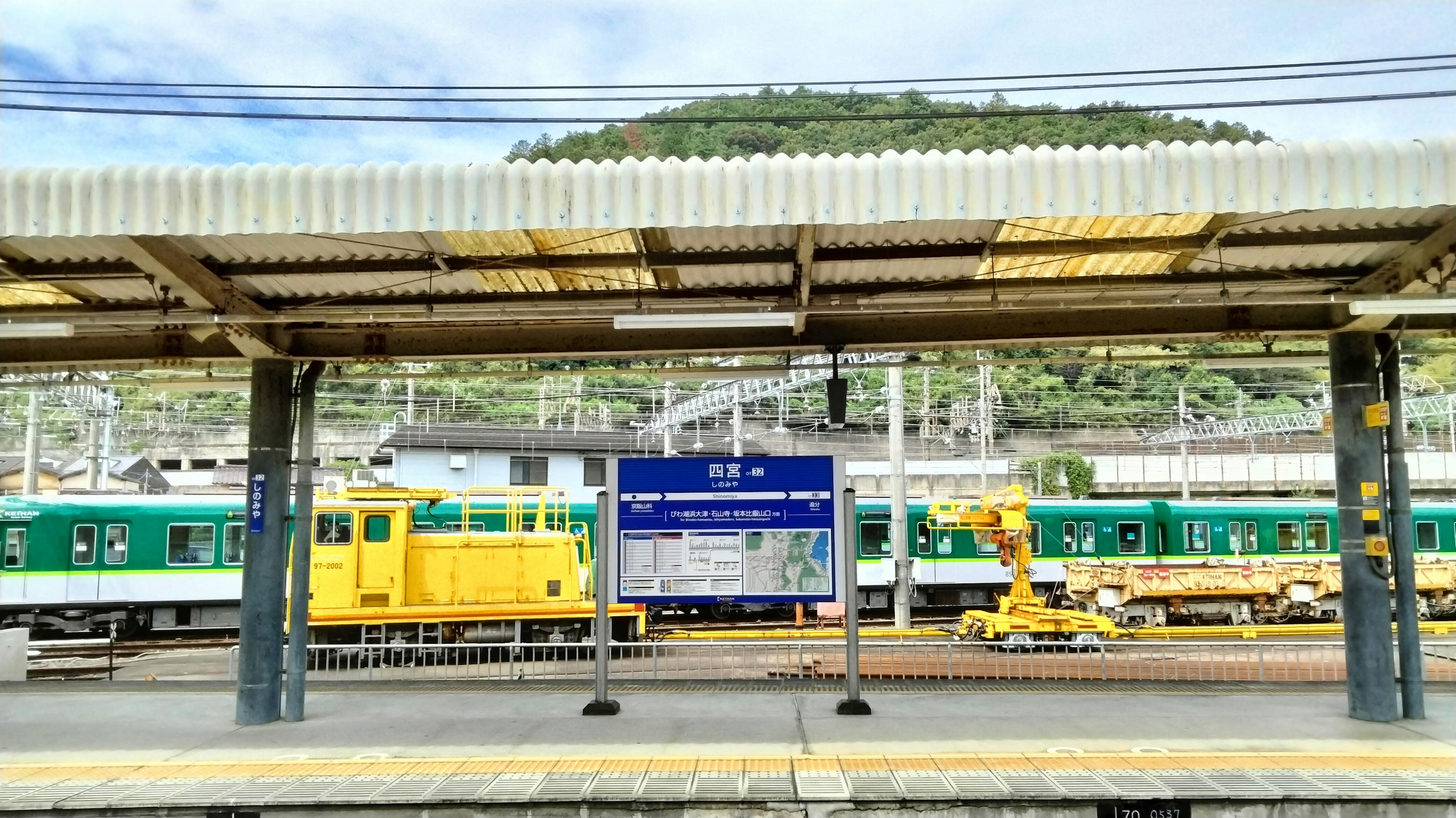 Train station platform with green and yellow trains and a mountain in the background