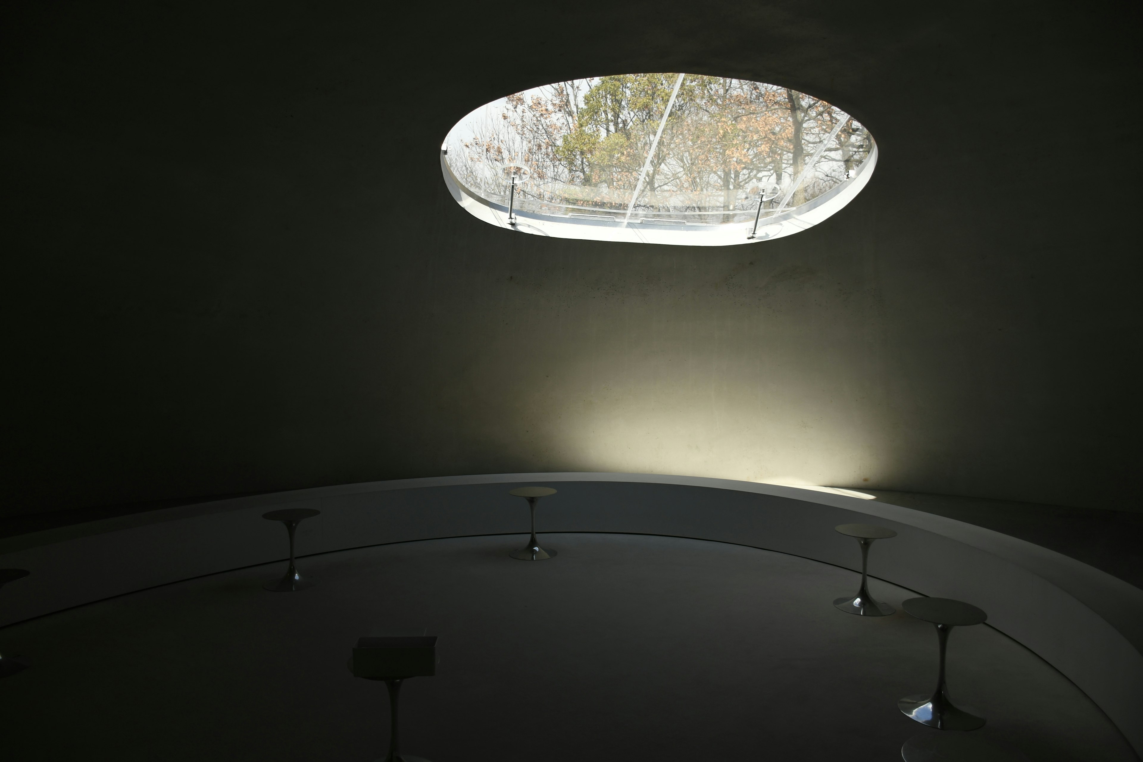 A circular space with an oval window allowing natural light to enter a minimalist interior