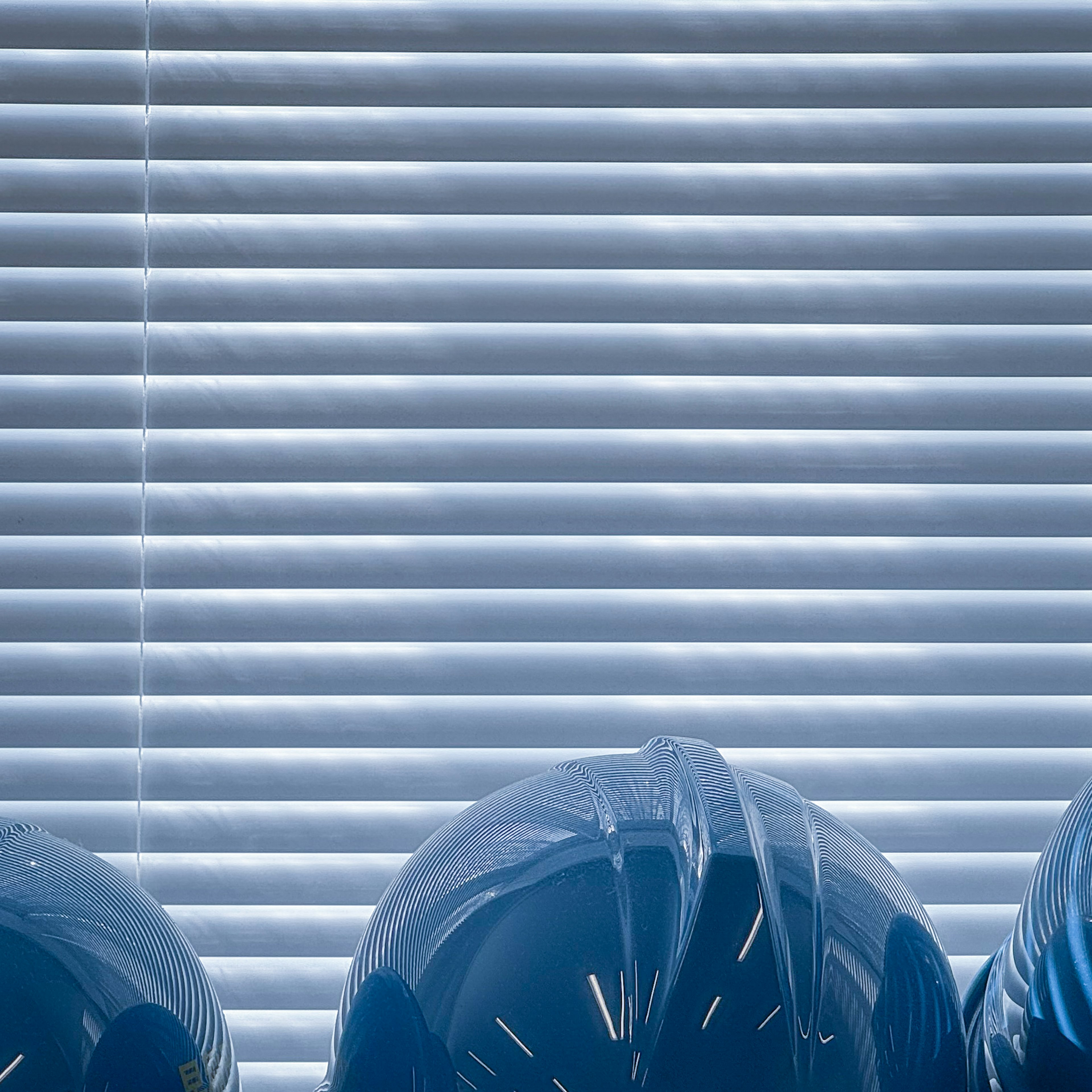 Three blue balloons positioned in front of window blinds