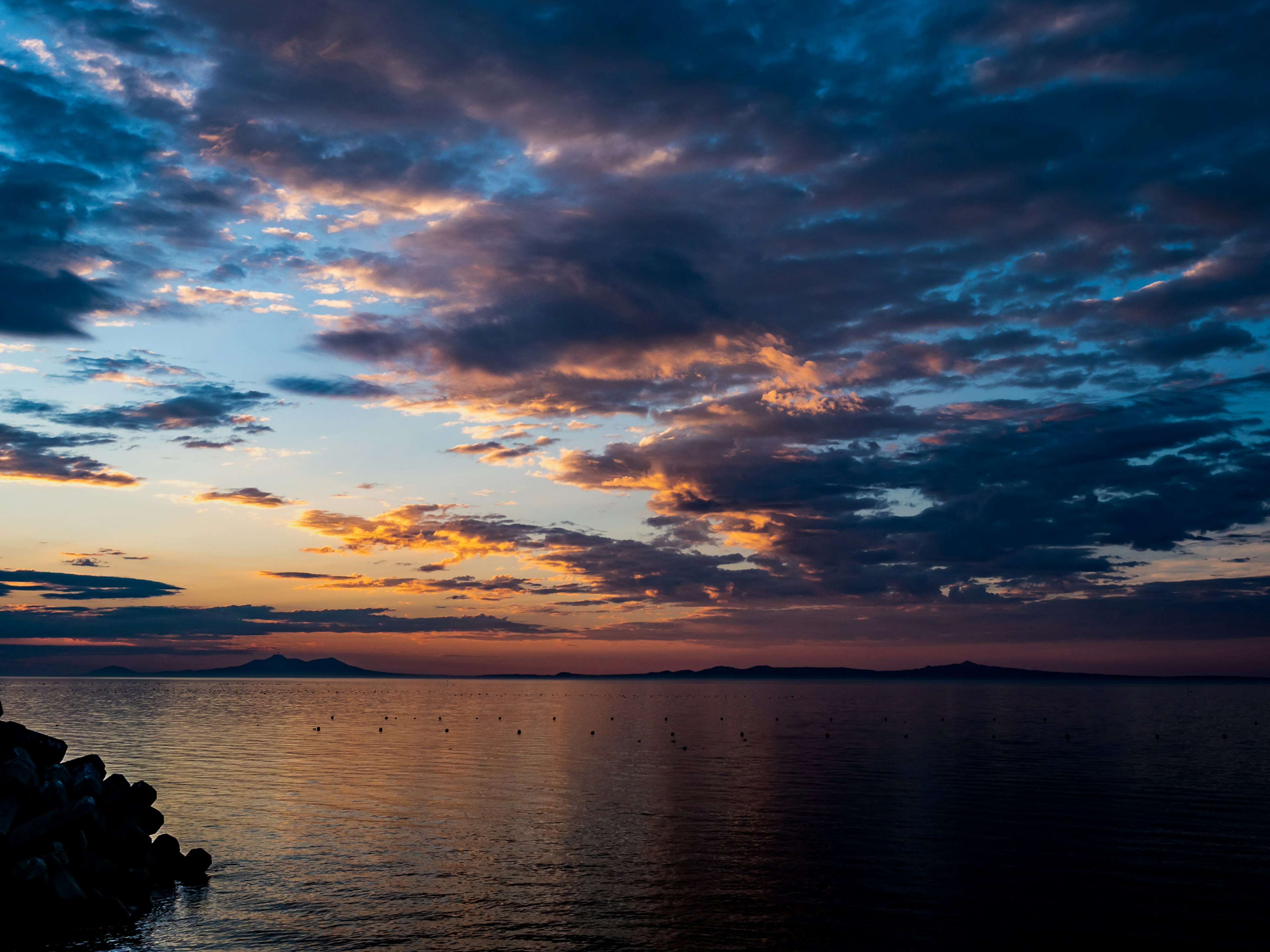 Sereno atardecer sobre aguas tranquilas con nubes dramáticas