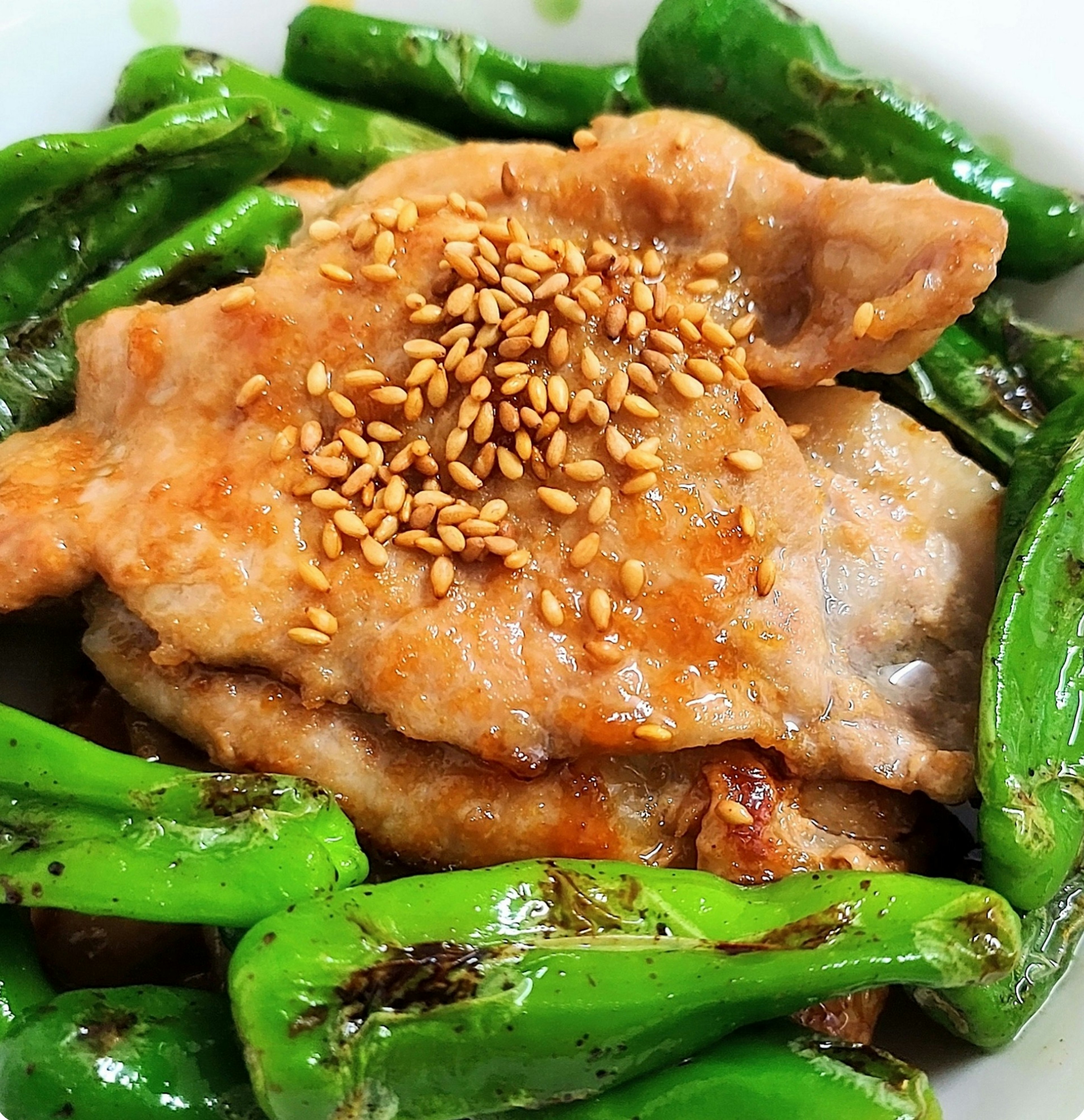 Dish of chicken topped with sesame seeds served with green peppers