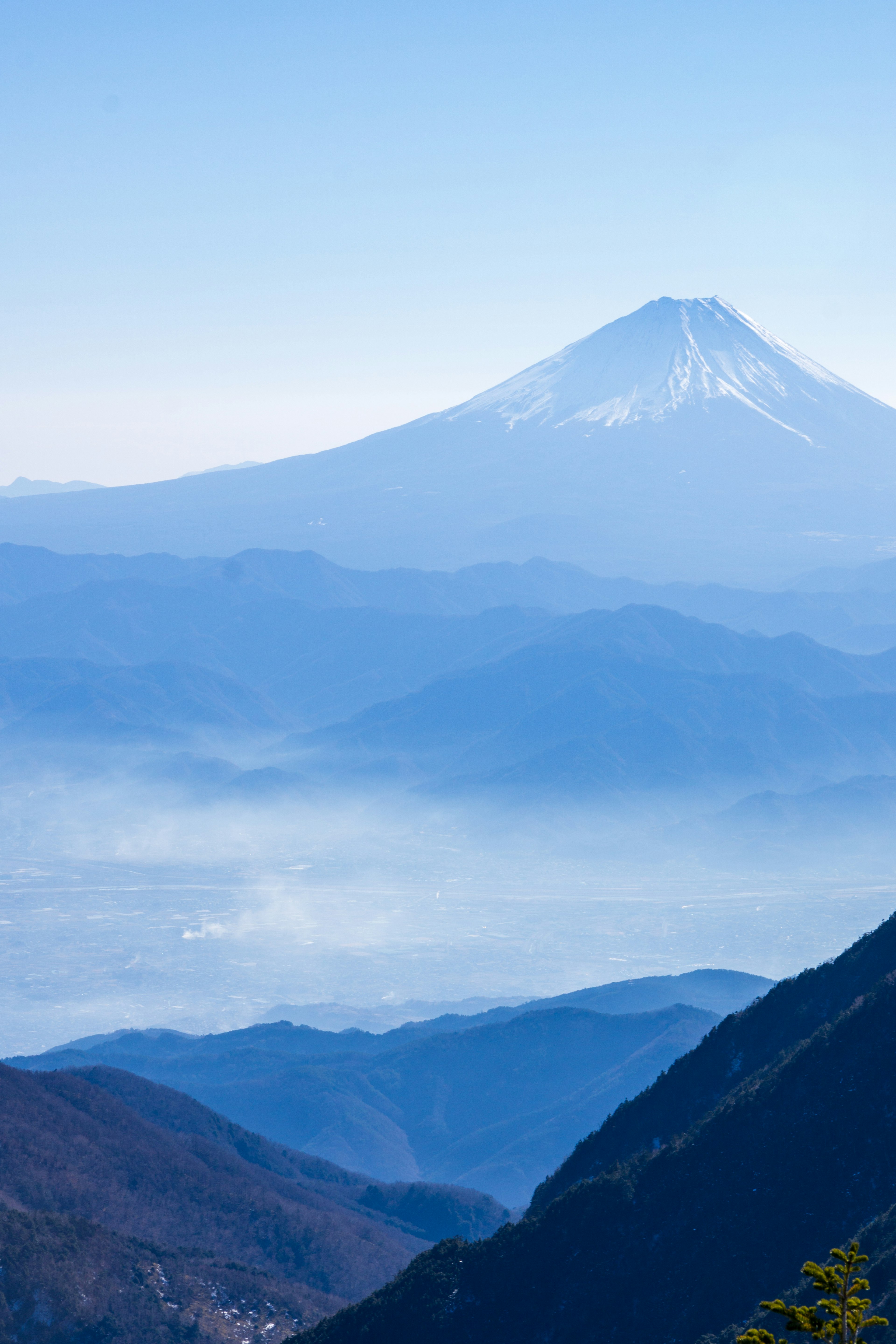 Le mont Fuji se dresse sous un ciel bleu avec des montagnes environnantes enveloppées de brume