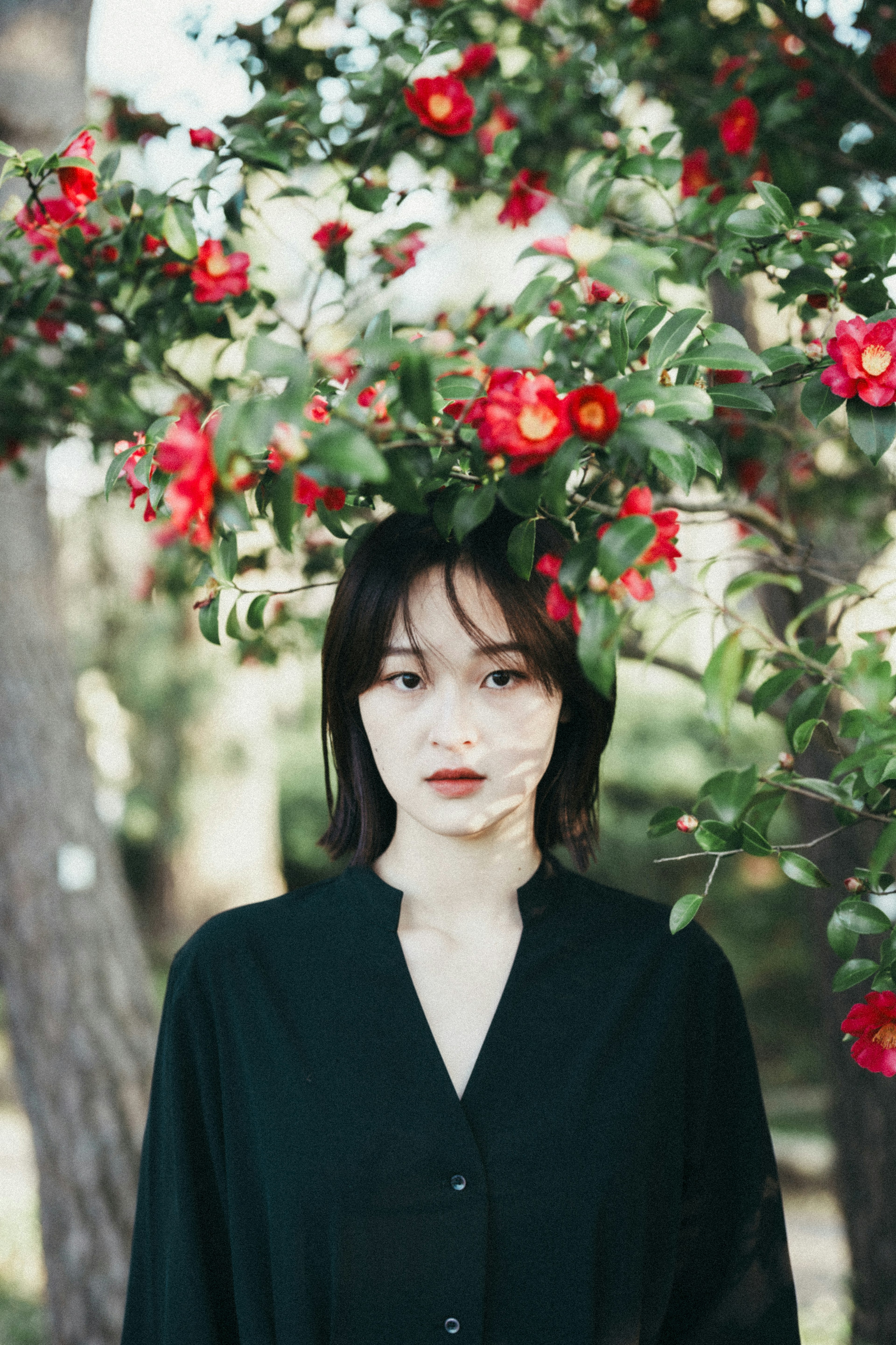 Retrato de una mujer de pie frente a un árbol con flores rojas