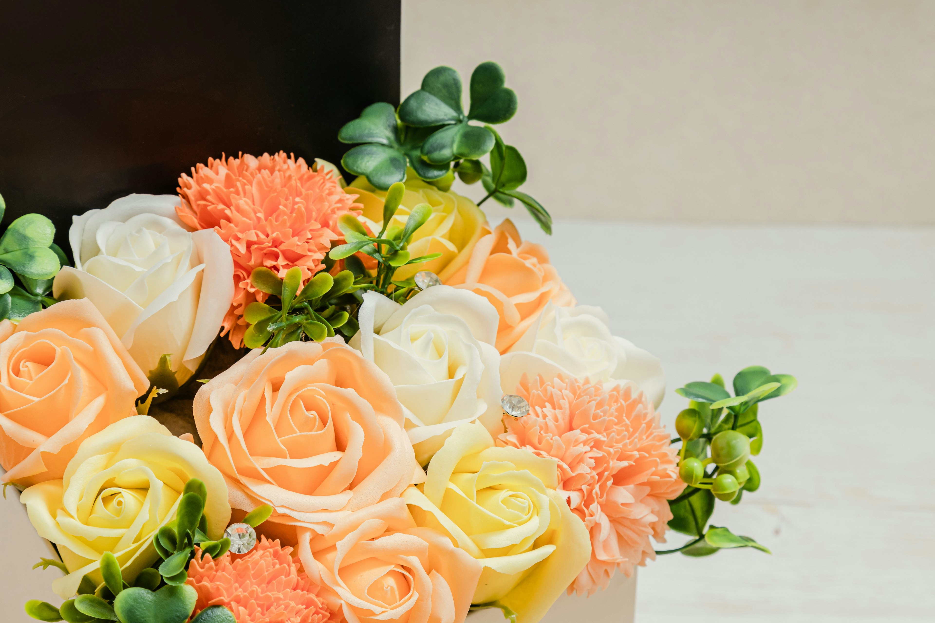 Strauß aus Pfirsich- und weißen Rosen mit Nelken in einer schwarzen Box angeordnet