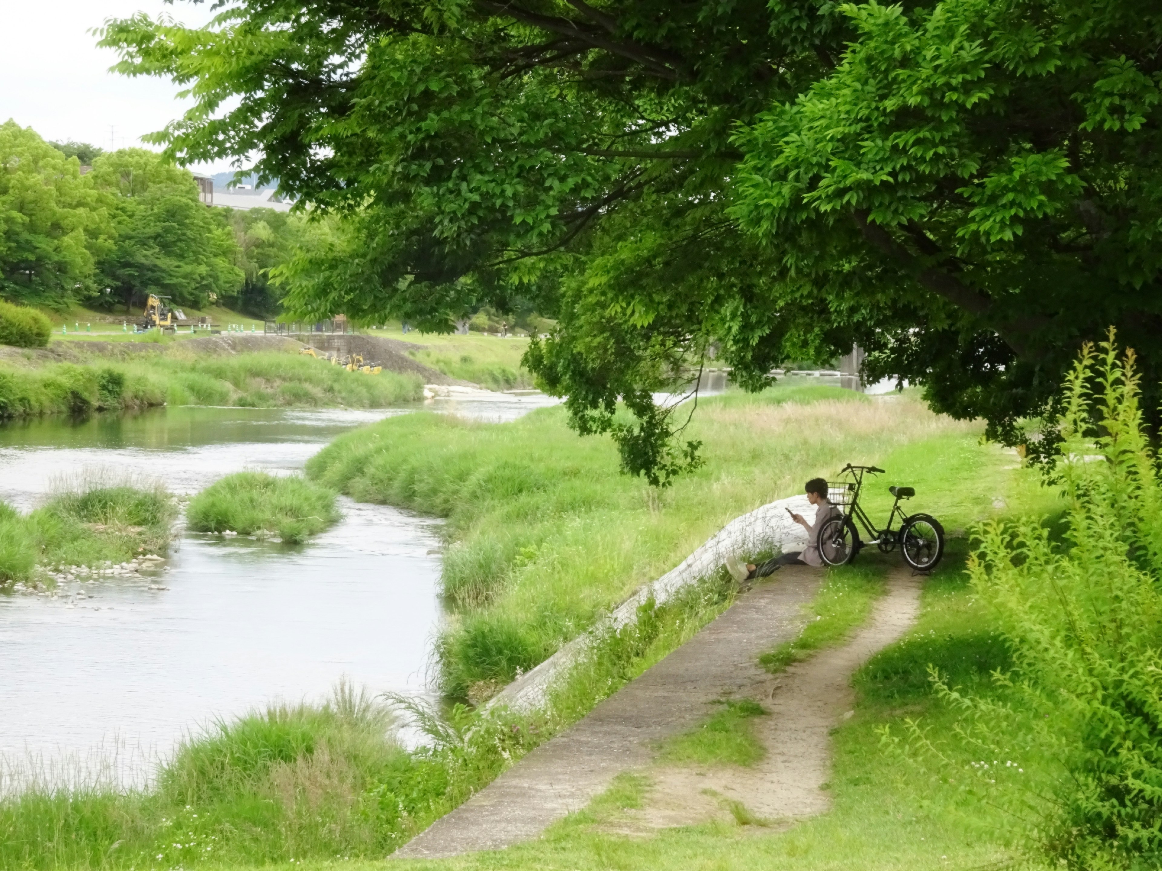 Une personne se reposant au bord d'une rivière avec un vélo sur un chemin verdoyant