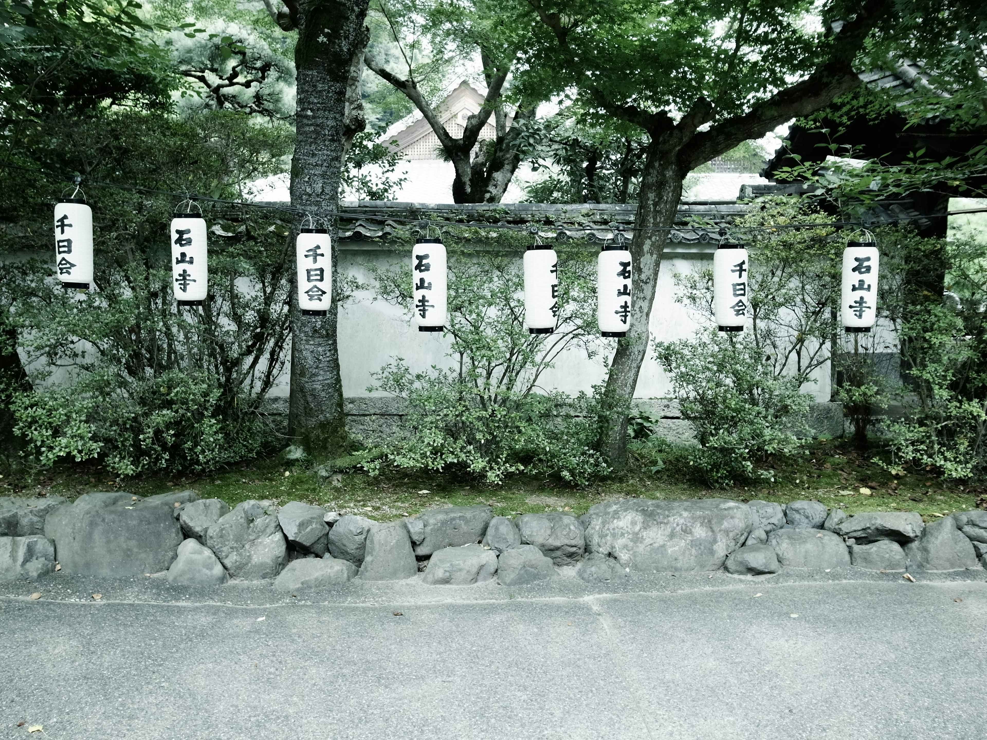 石の壁と緑の木々に囲まれた日本の庭園の風景と、書かれた看板が並ぶ