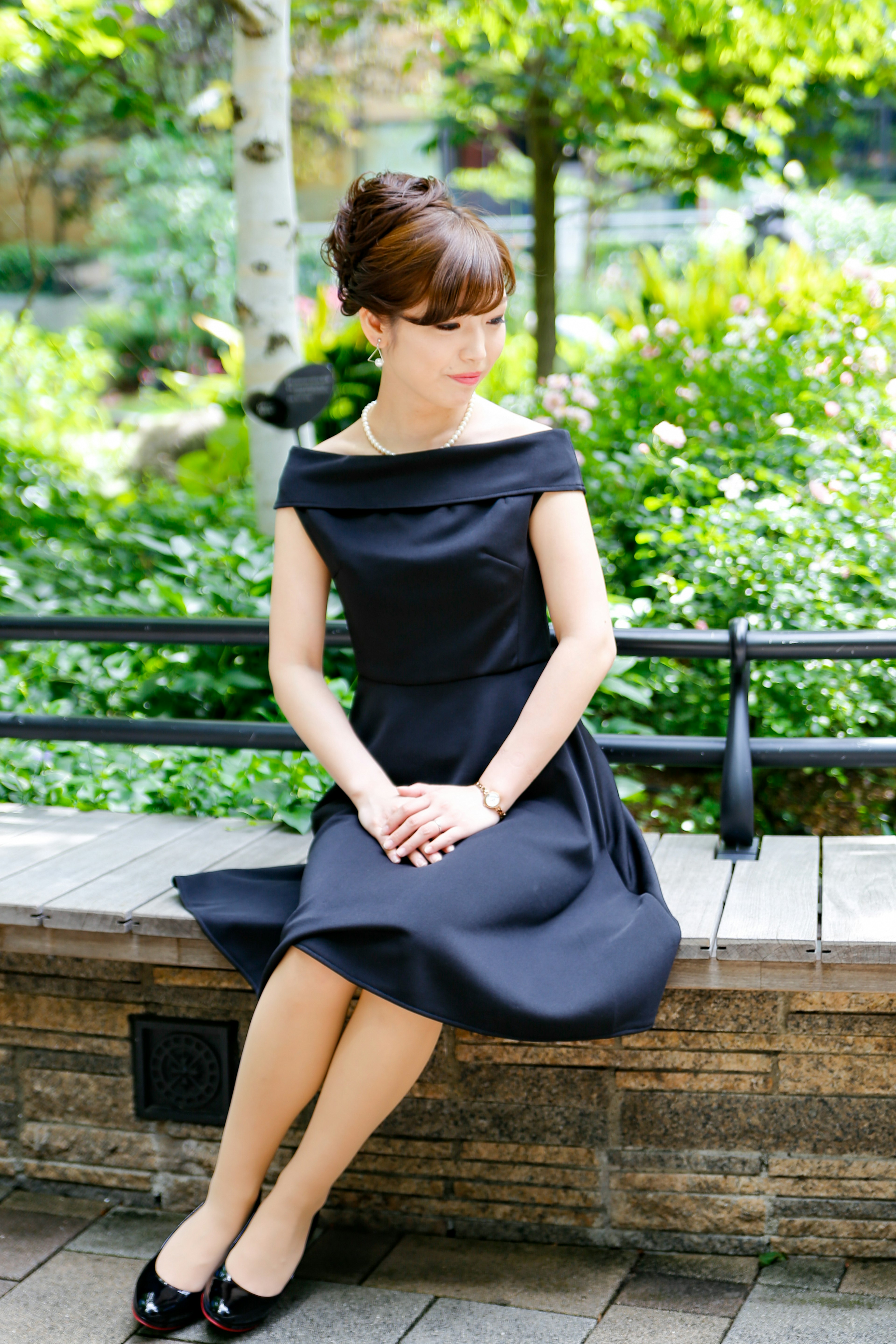 A woman in a black dress sitting on a bench in a park with a green background