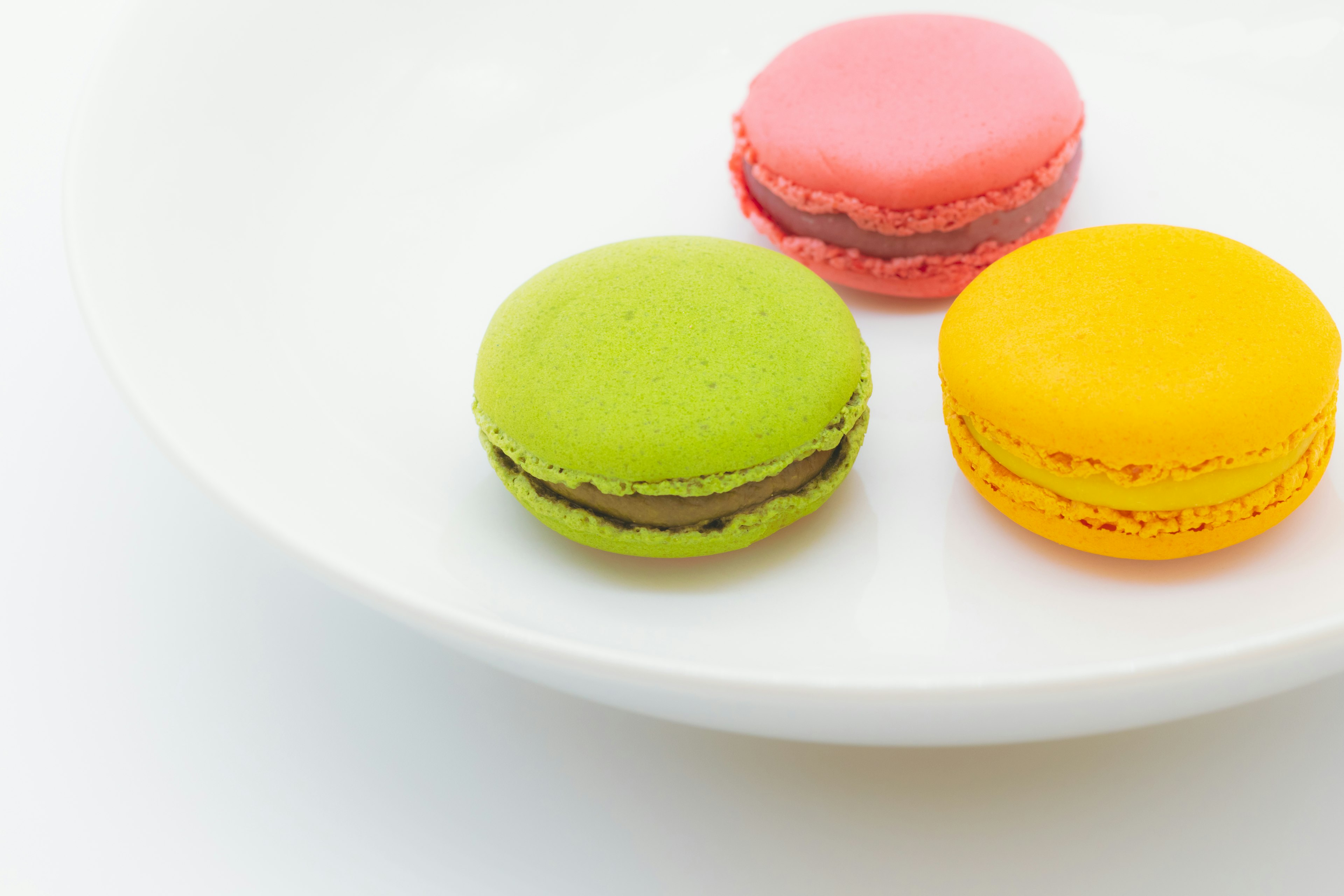 Green pink and yellow macarons arranged on a white plate