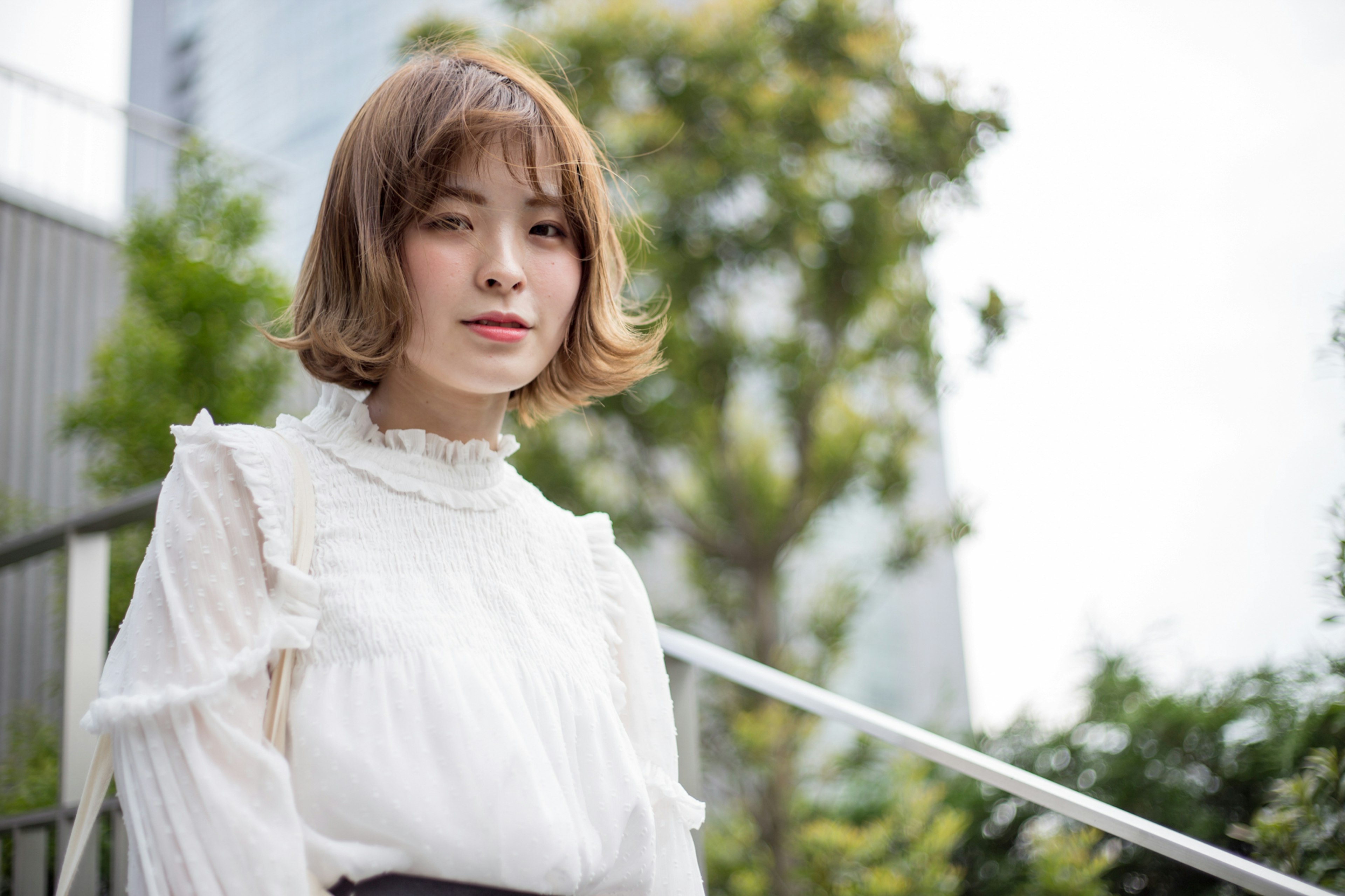 Young woman in a white blouse standing on stairs with green trees in the background