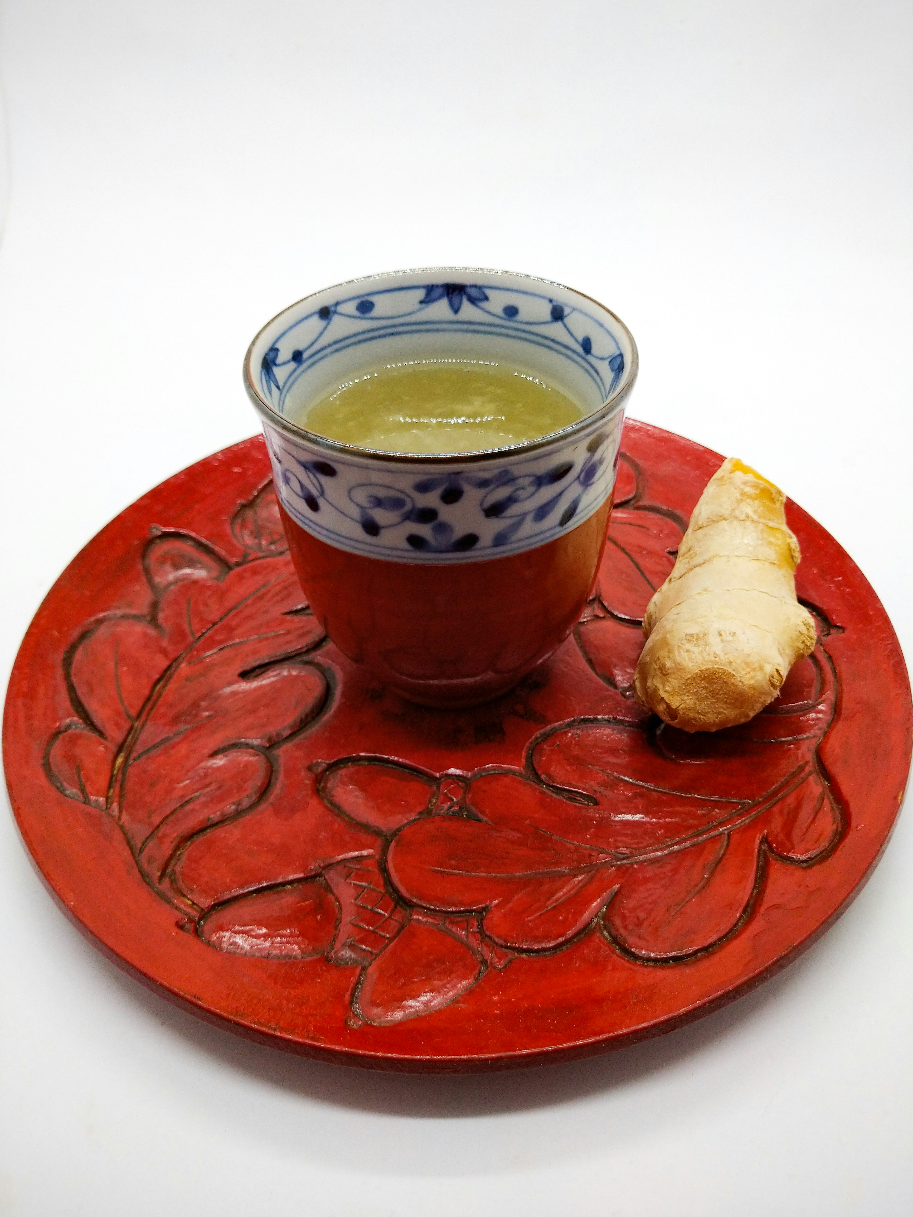 A cup of green tea on a red plate with a piece of ginger