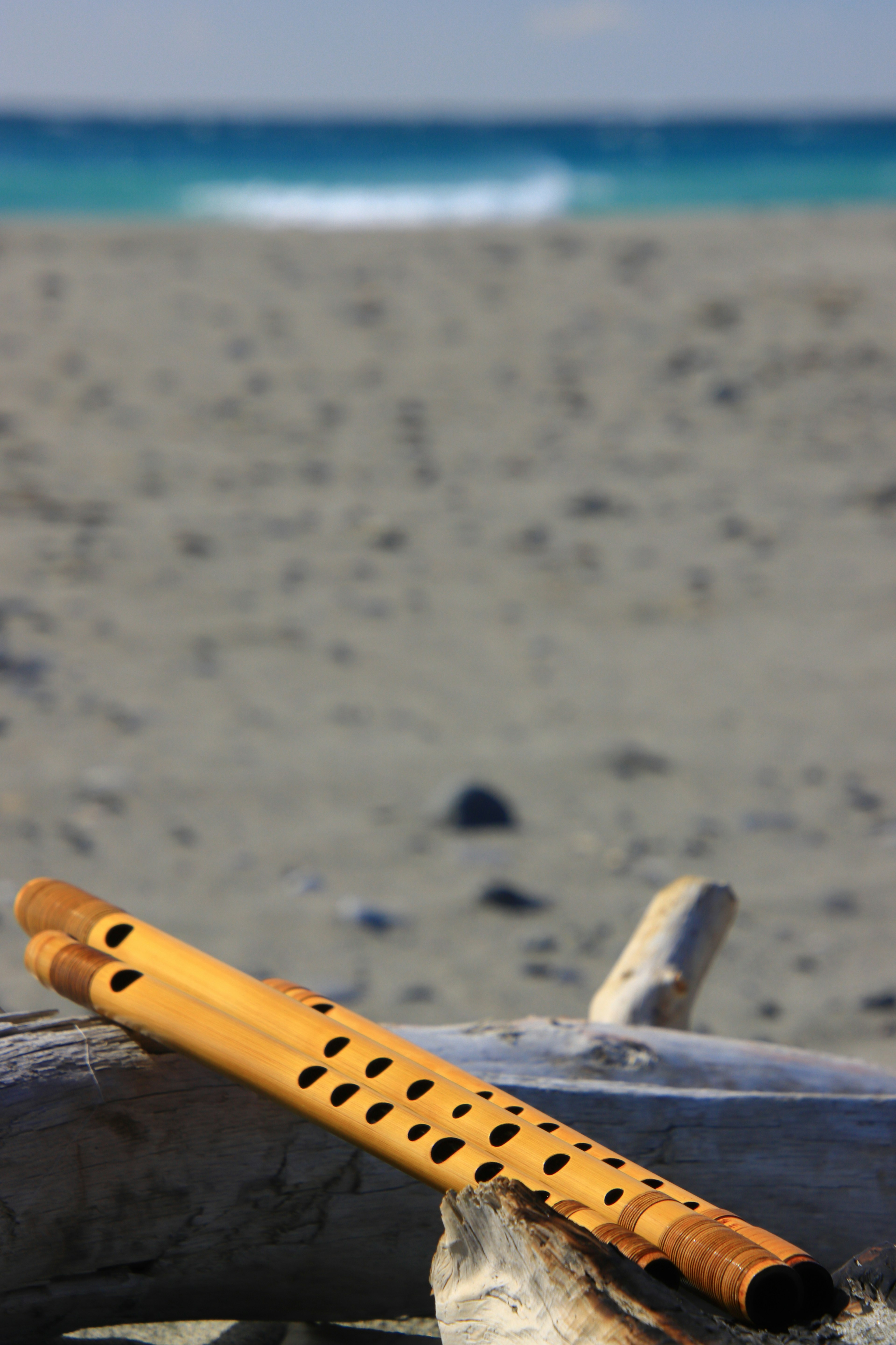 Wooden flute resting on the beach with a blue ocean background