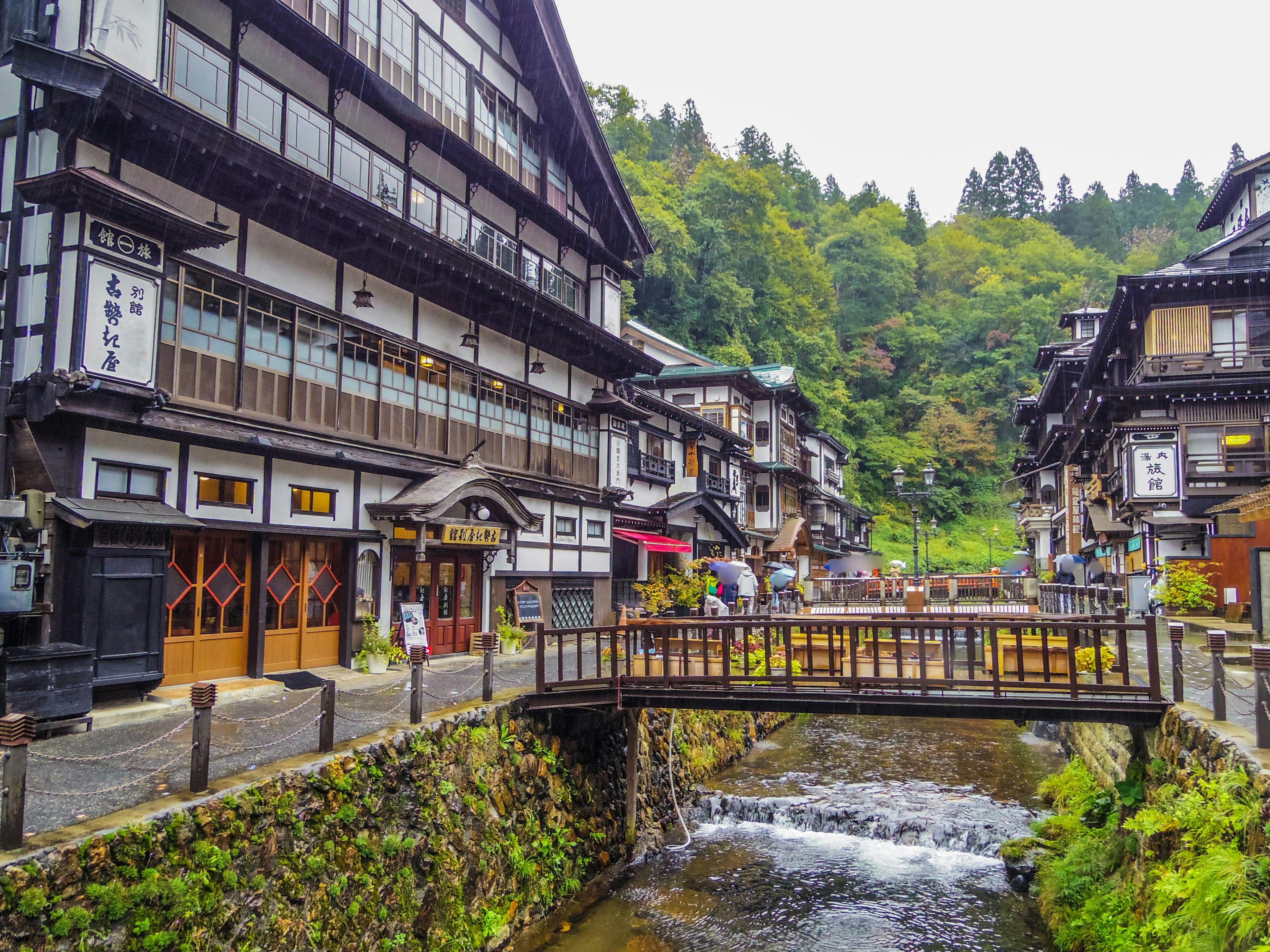 Scenic view of a historic hot spring town with traditional buildings a bridge and a river surrounded by lush greenery