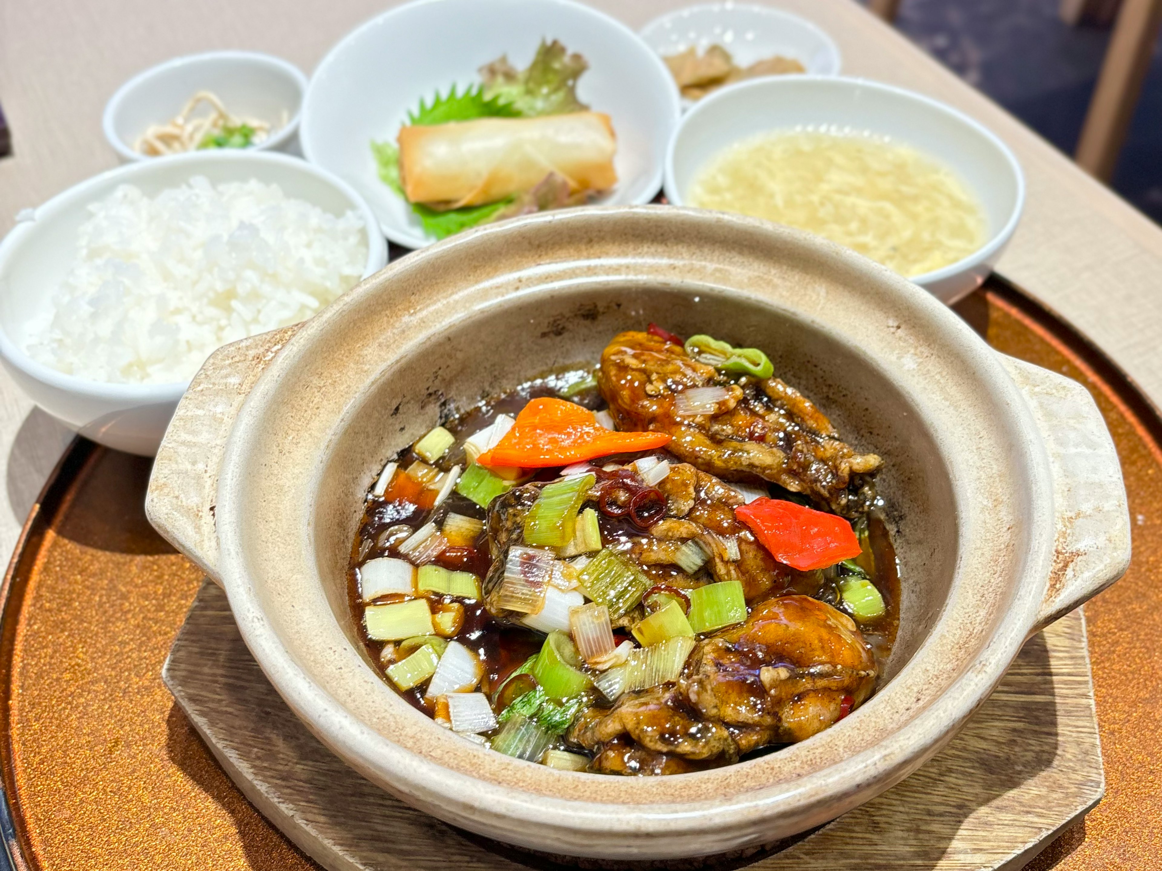 Hot pot of chicken and vegetables served in a clay bowl with side dishes including rice and spring rolls