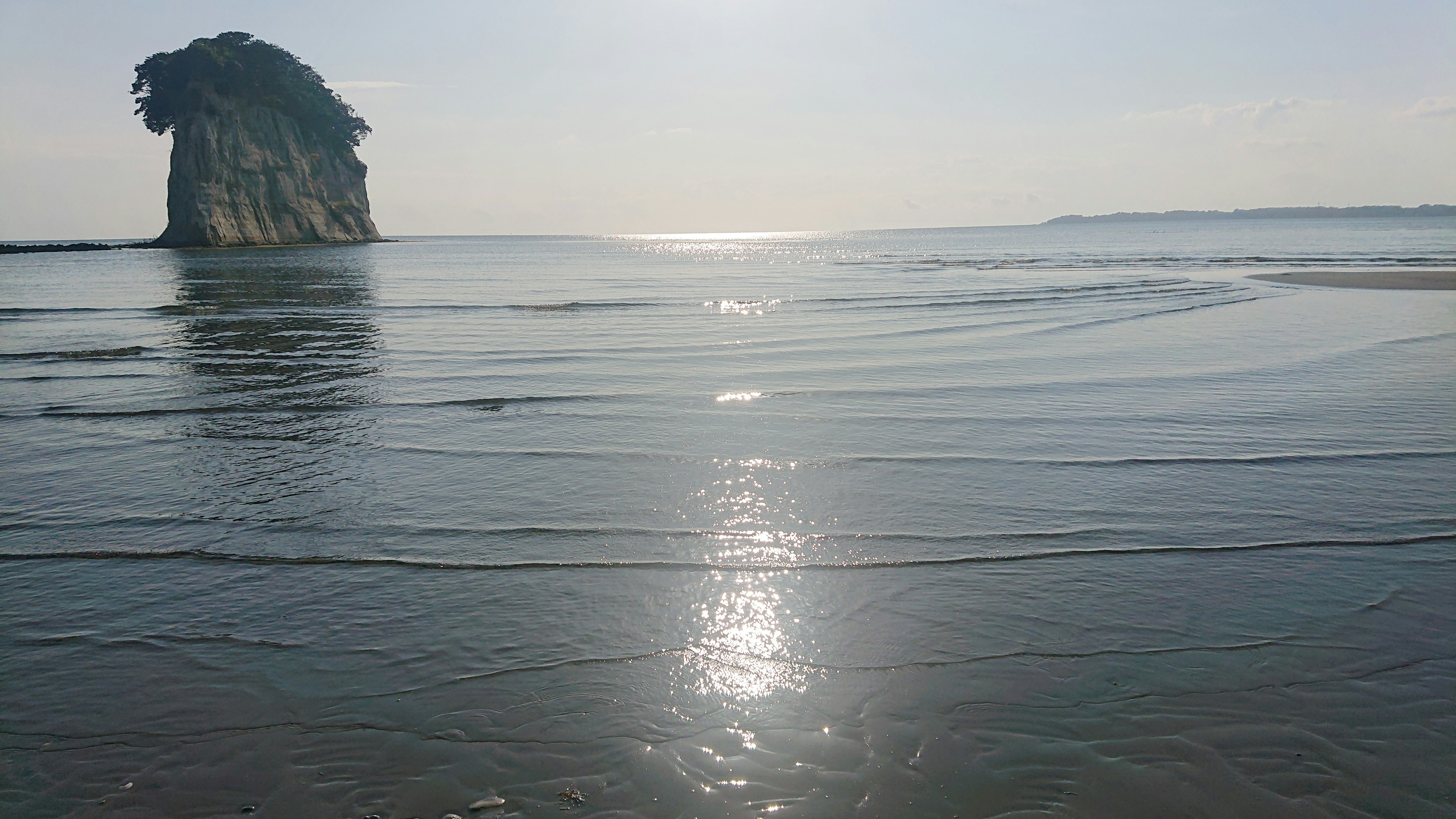 Pemandangan pantai yang tenang dengan air berkilau laut biru dan pulau berbatu