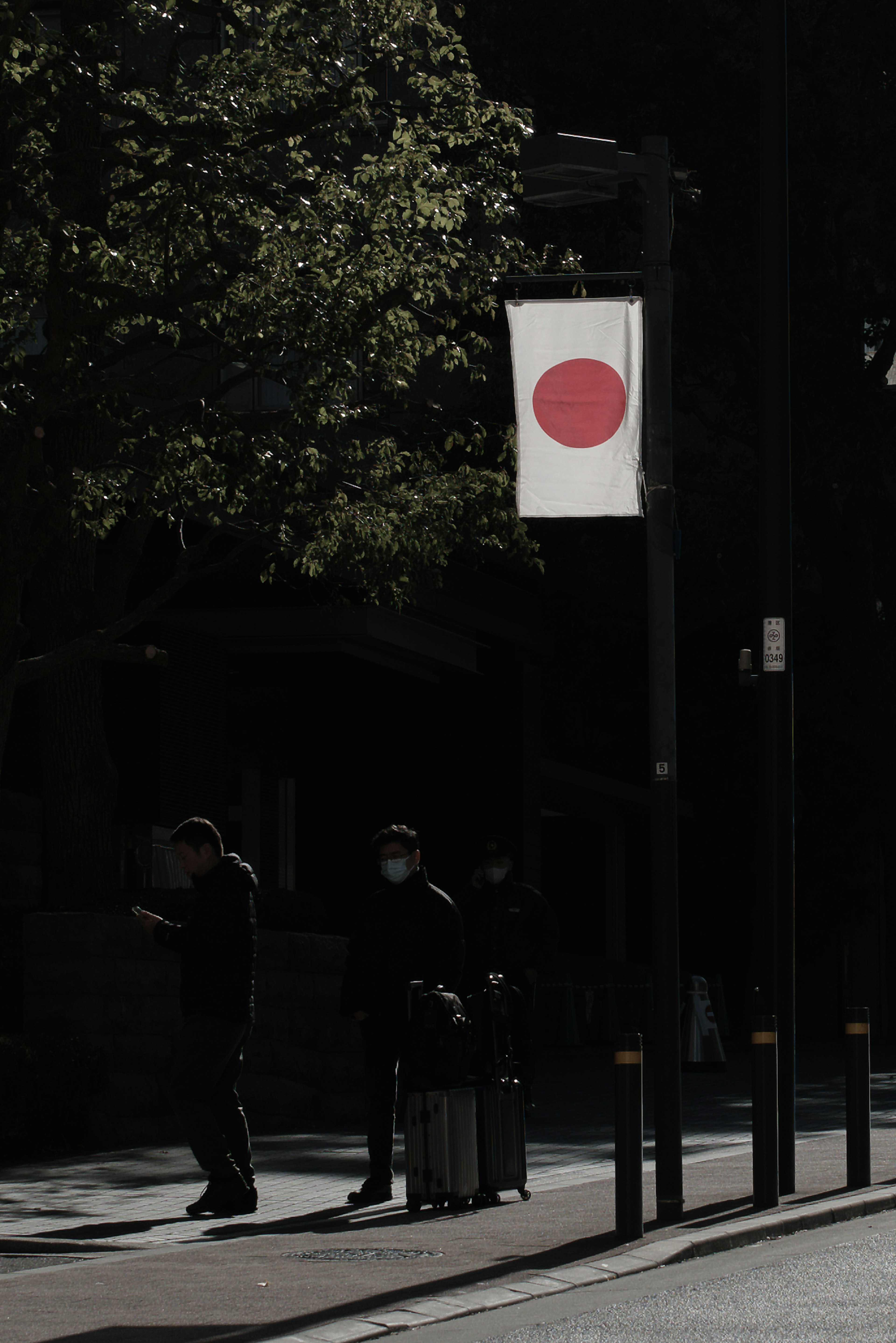 Silueta de personas en una esquina de la calle con la bandera japonesa exhibida contra un fondo oscuro